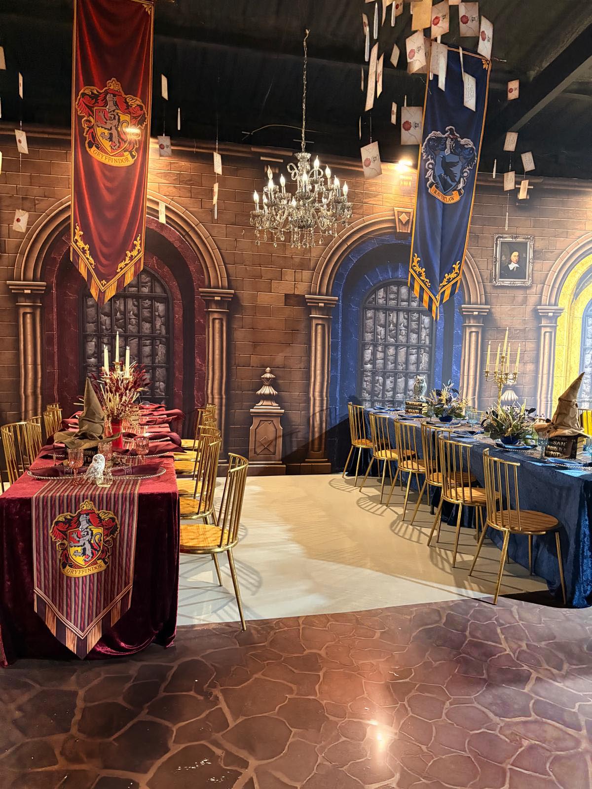 Decorated banquet hall with Harry Potter-themed banners, chandeliers, and long tables with chairs, set for an event.