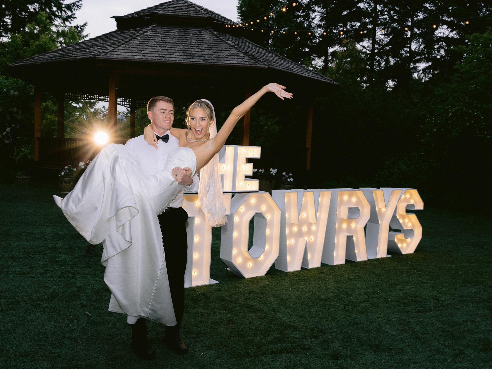 Couple dancing outdoors at night with illuminated letters spelling 'TOWYS' behind them.
