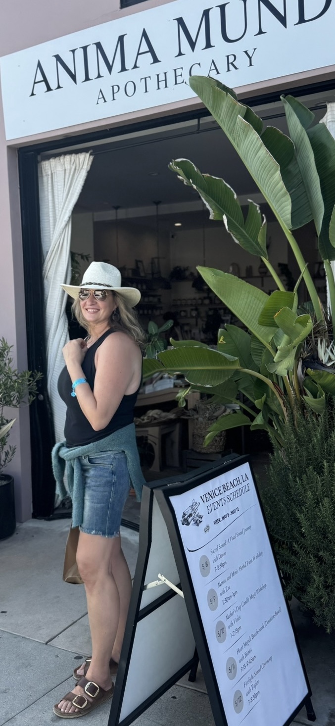 Woman in hat and denim shorts standing outside pharmacy with large plant and menu board