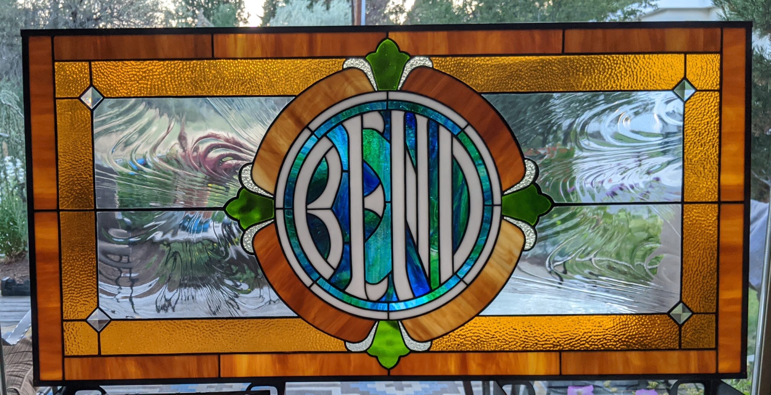 Stained glass window with the word 'BEND' in the center, surrounded by geometric patterns and colors.