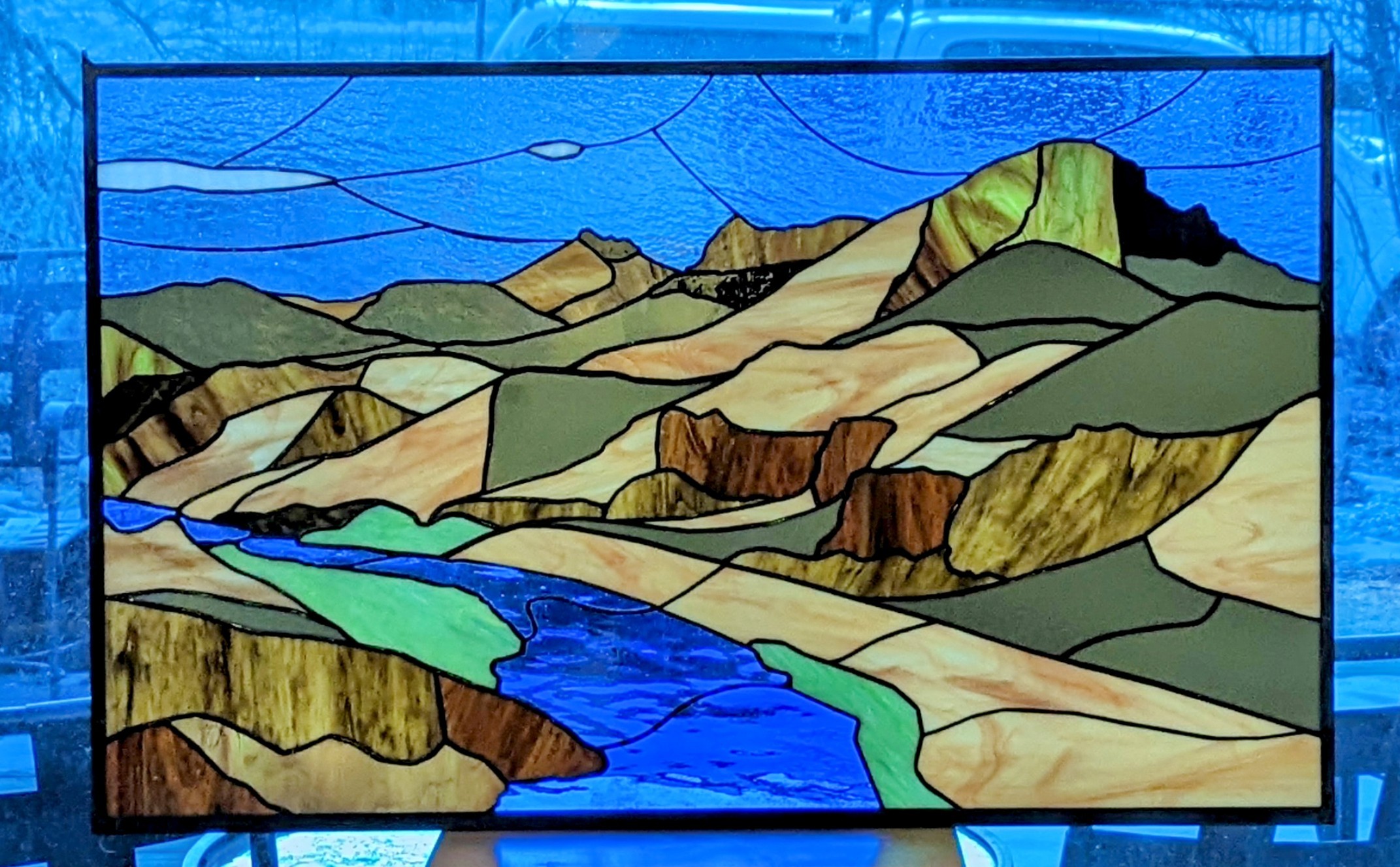 Colorful stained glass landscape with mountains, river, and sky, depicted in a stylized, abstract manner.