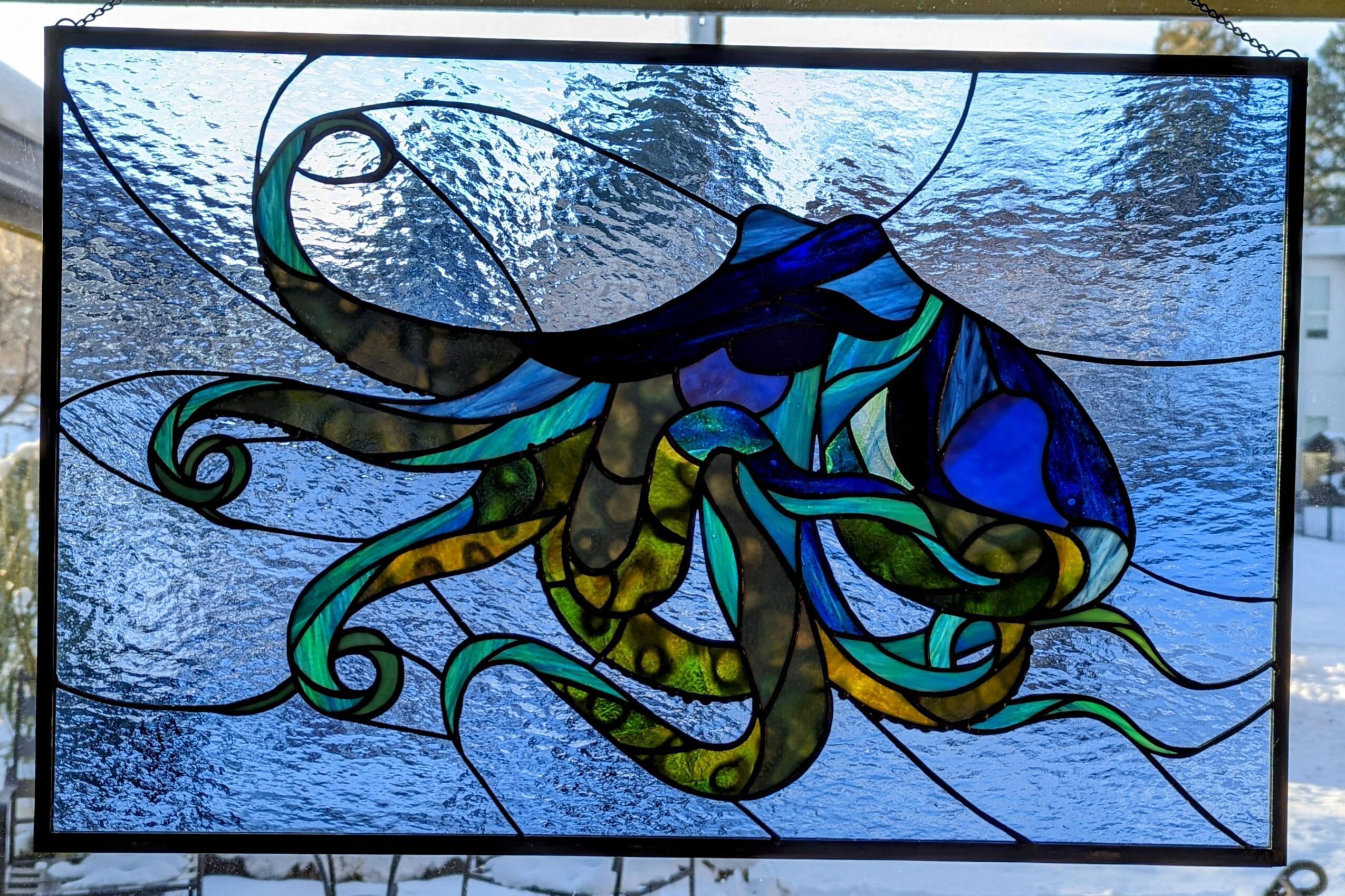 Stained glass window with an abstract design of swirling shapes in blue, green, and yellow colors.