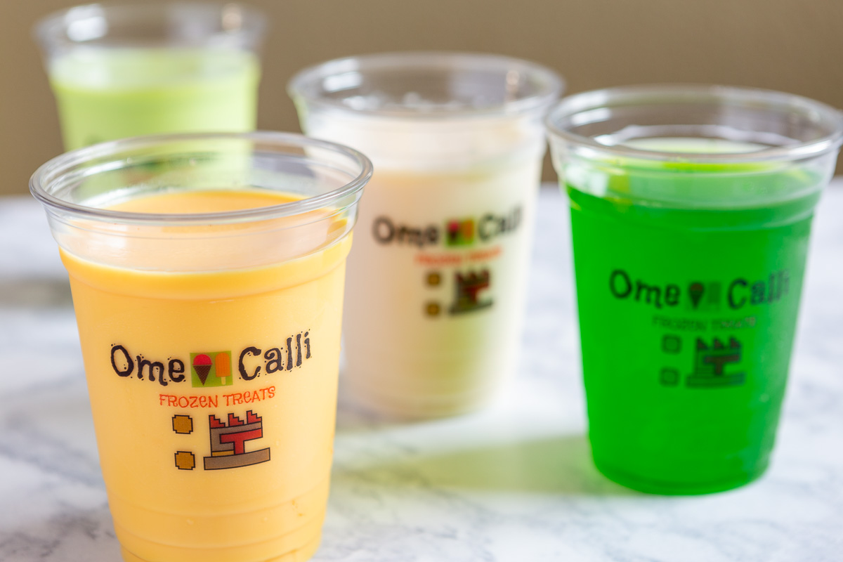 Four colorful drinks in clear cups with logos, placed on a wooden surface, with a blurred background.
