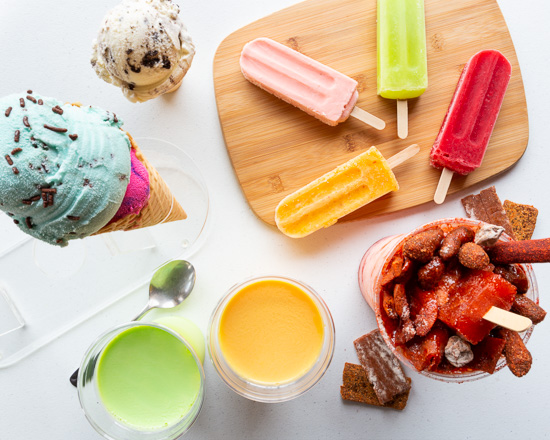 Ice cream cone, colorful popsicles, juice, and a bowl of candies on a table.