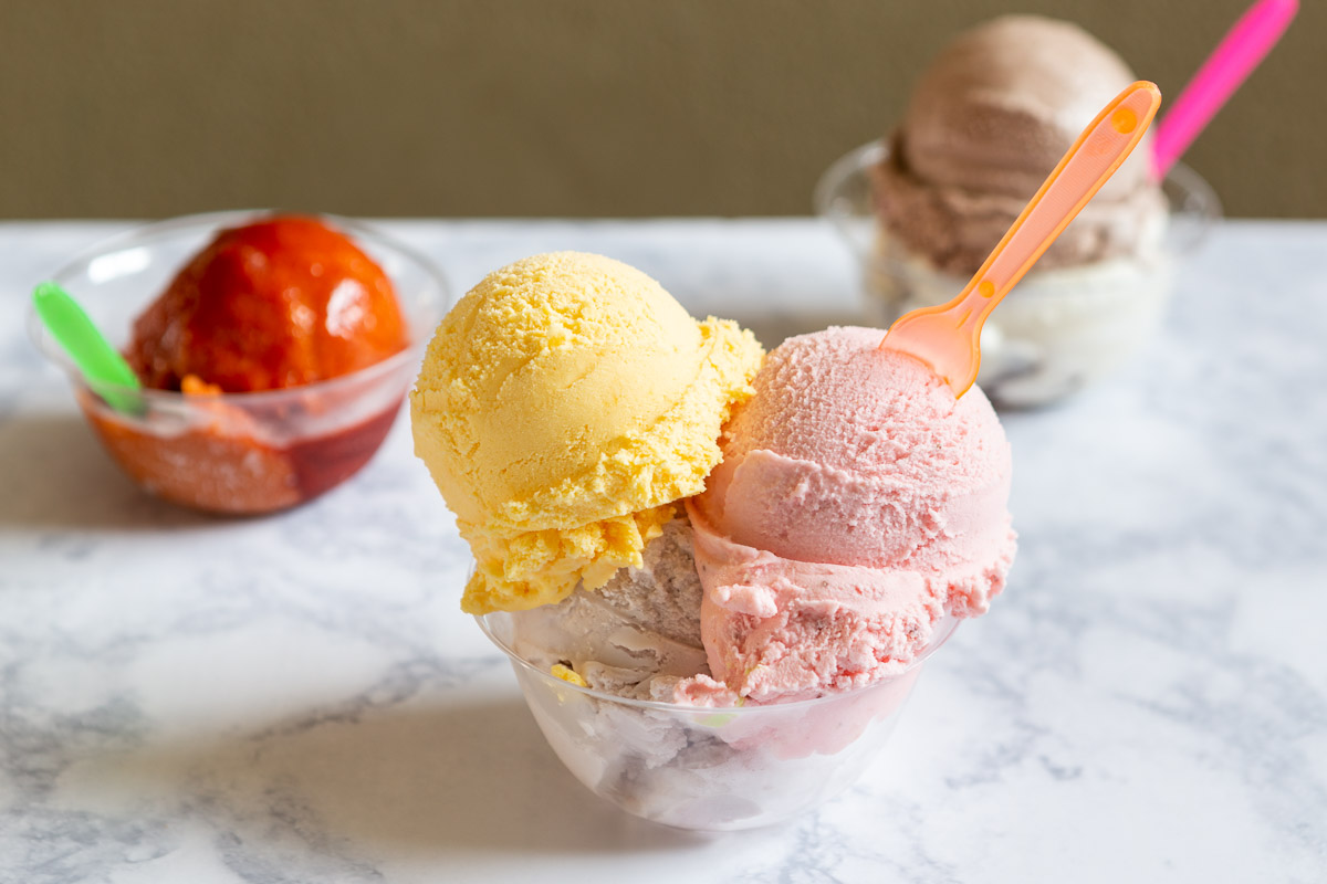 Two scoops of pink and yellow ice cream in a glass bowl on a marble surface.