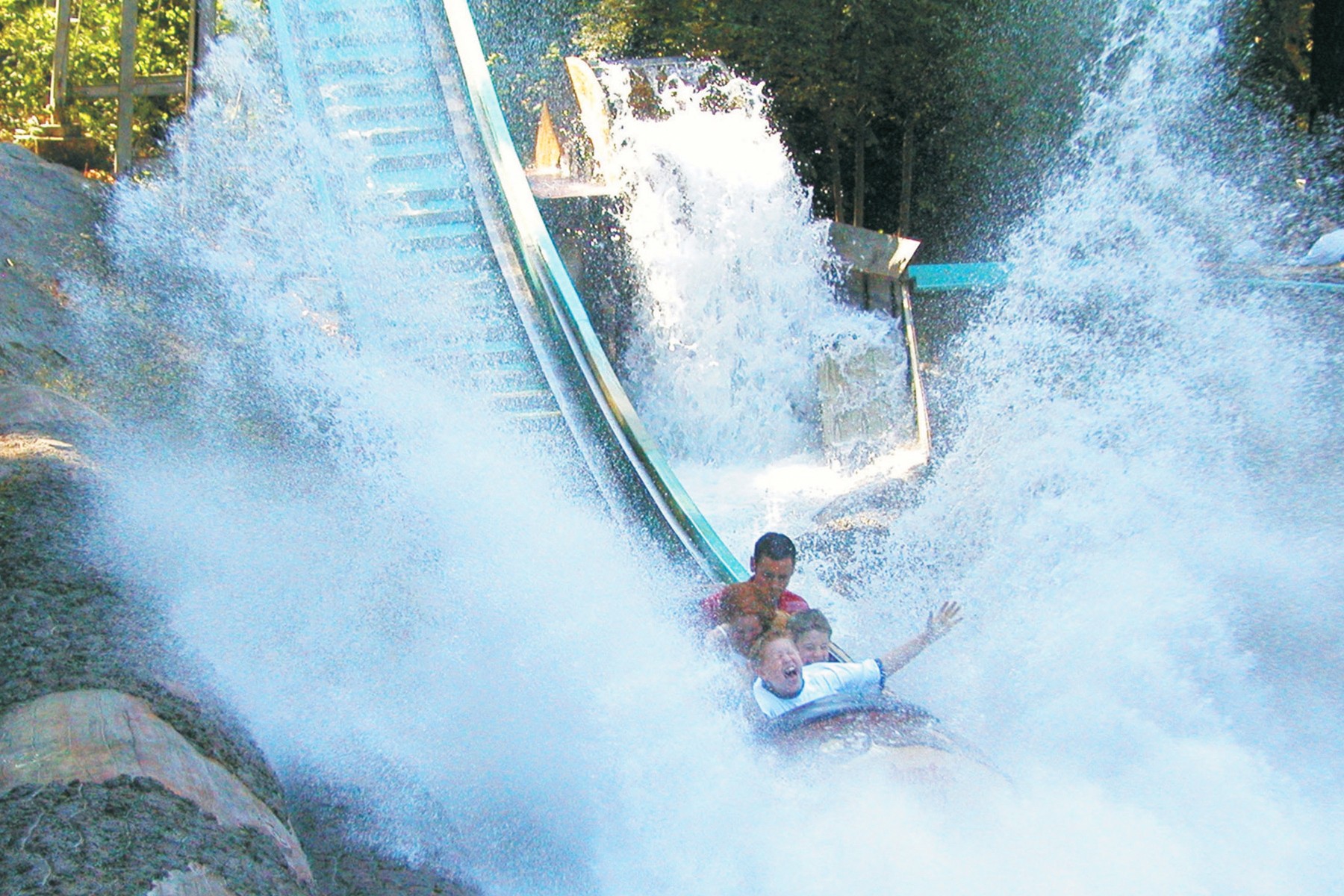 Person on a water slide with water splashing around, trees in the background.