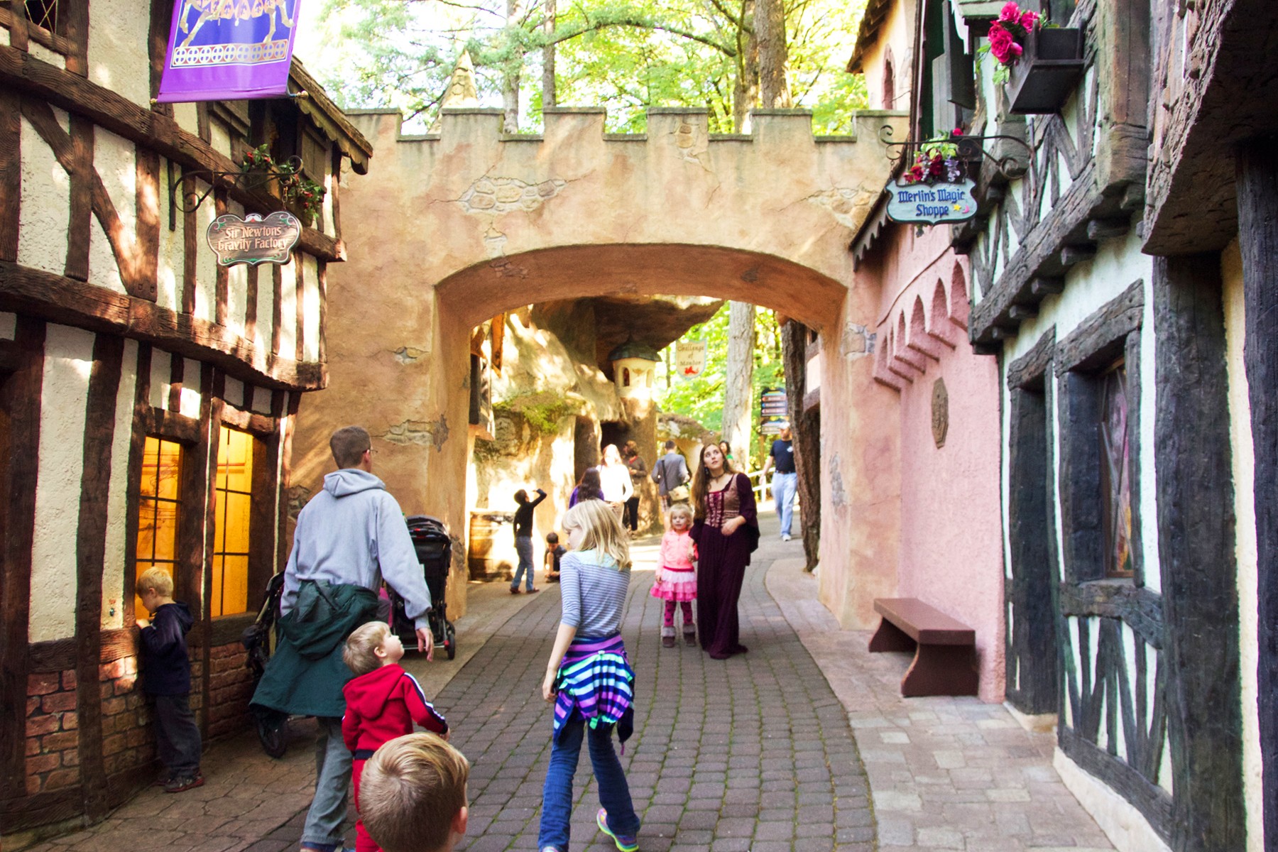 People walking through a narrow, cobblestone street with colorful buildings and an archway overhead, sunny day.