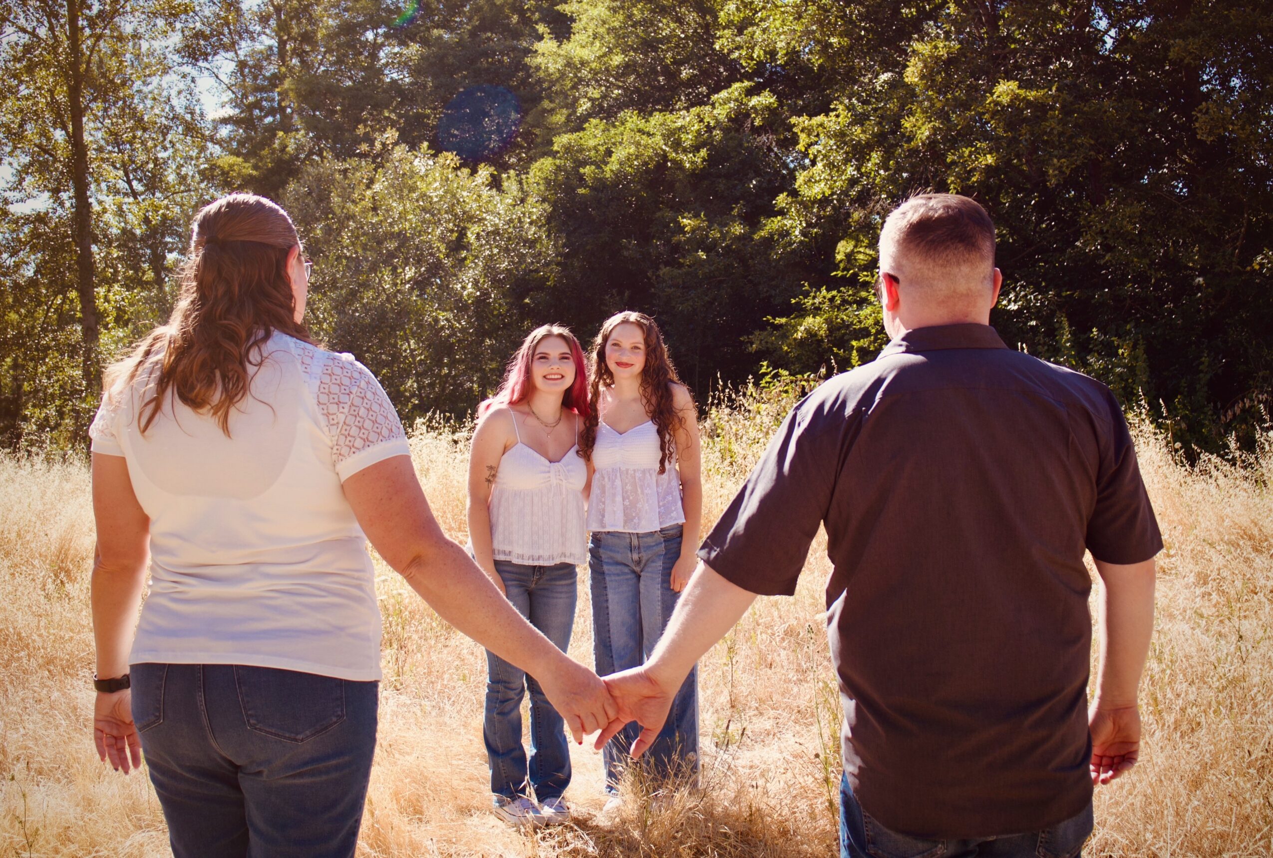 A couple holding hands facing two women in a field with trees in the background.
