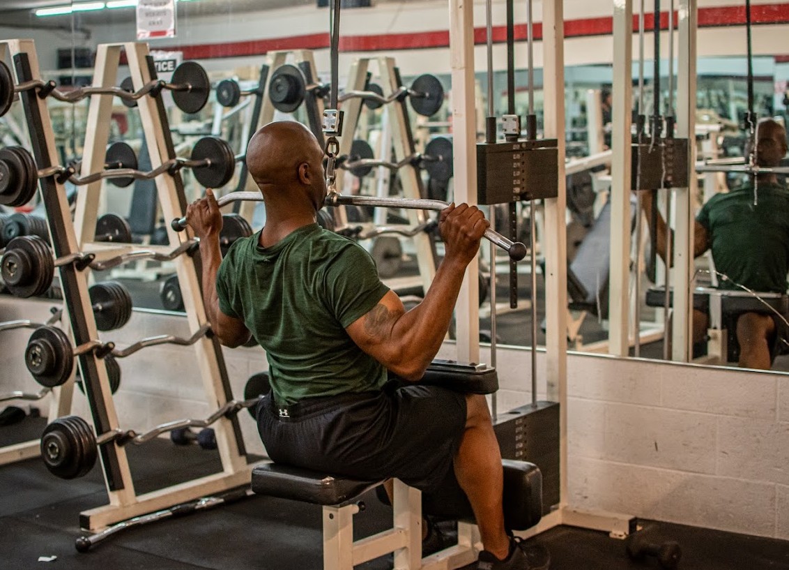 Man lifting weights in gym with mirrors and equipment around him.