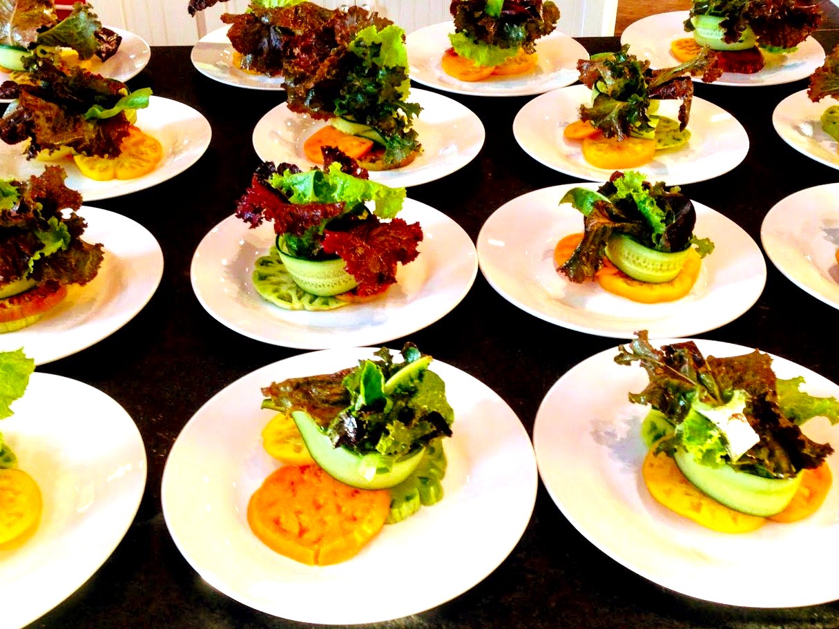 Multiple plates with small sandwiches topped with leafy greens and vegetables, arranged on a dark surface.