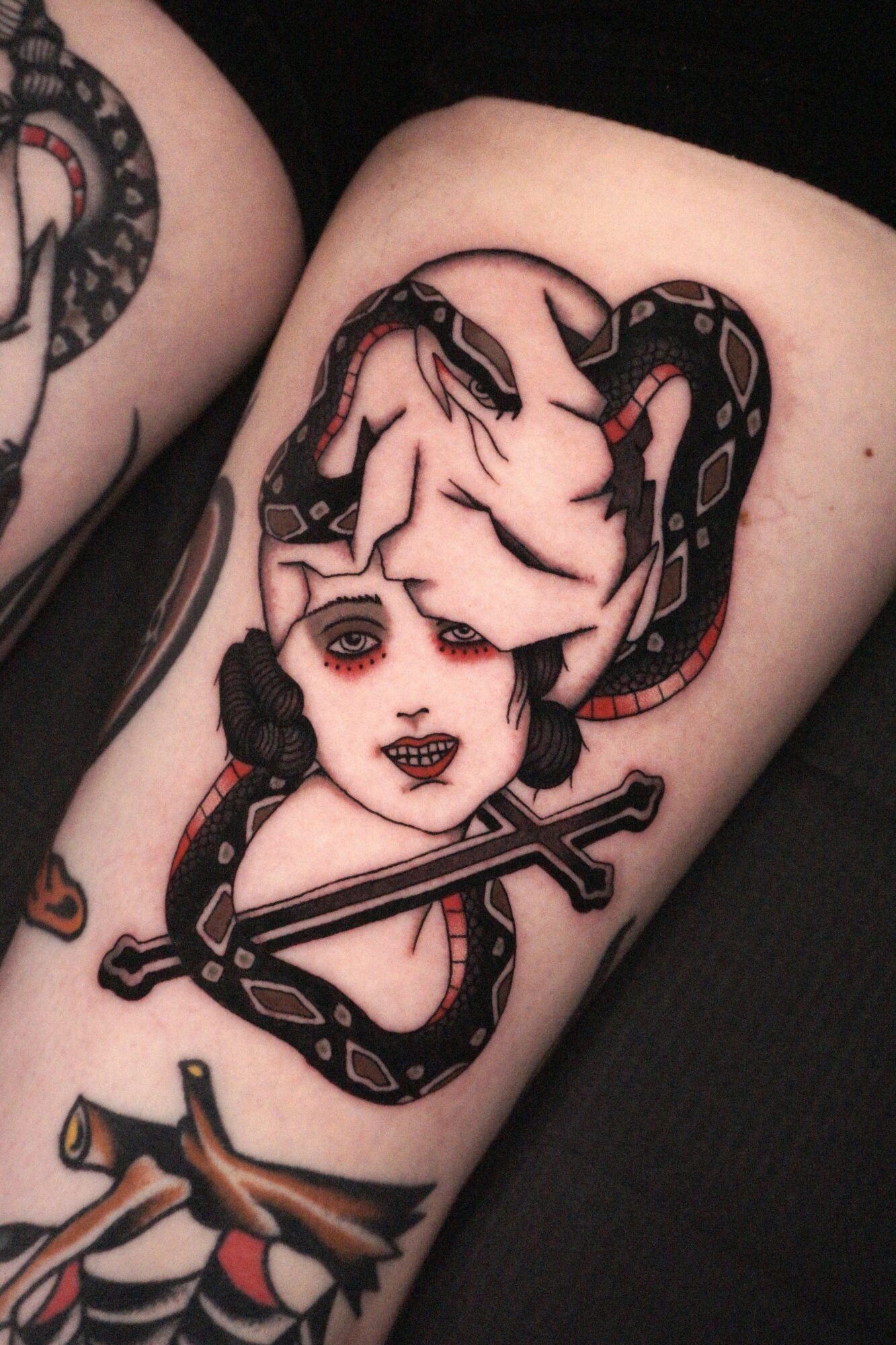 Tattoo of a woman with makeup and a snake wrapped around her head, holding a sword, on a person's arm.