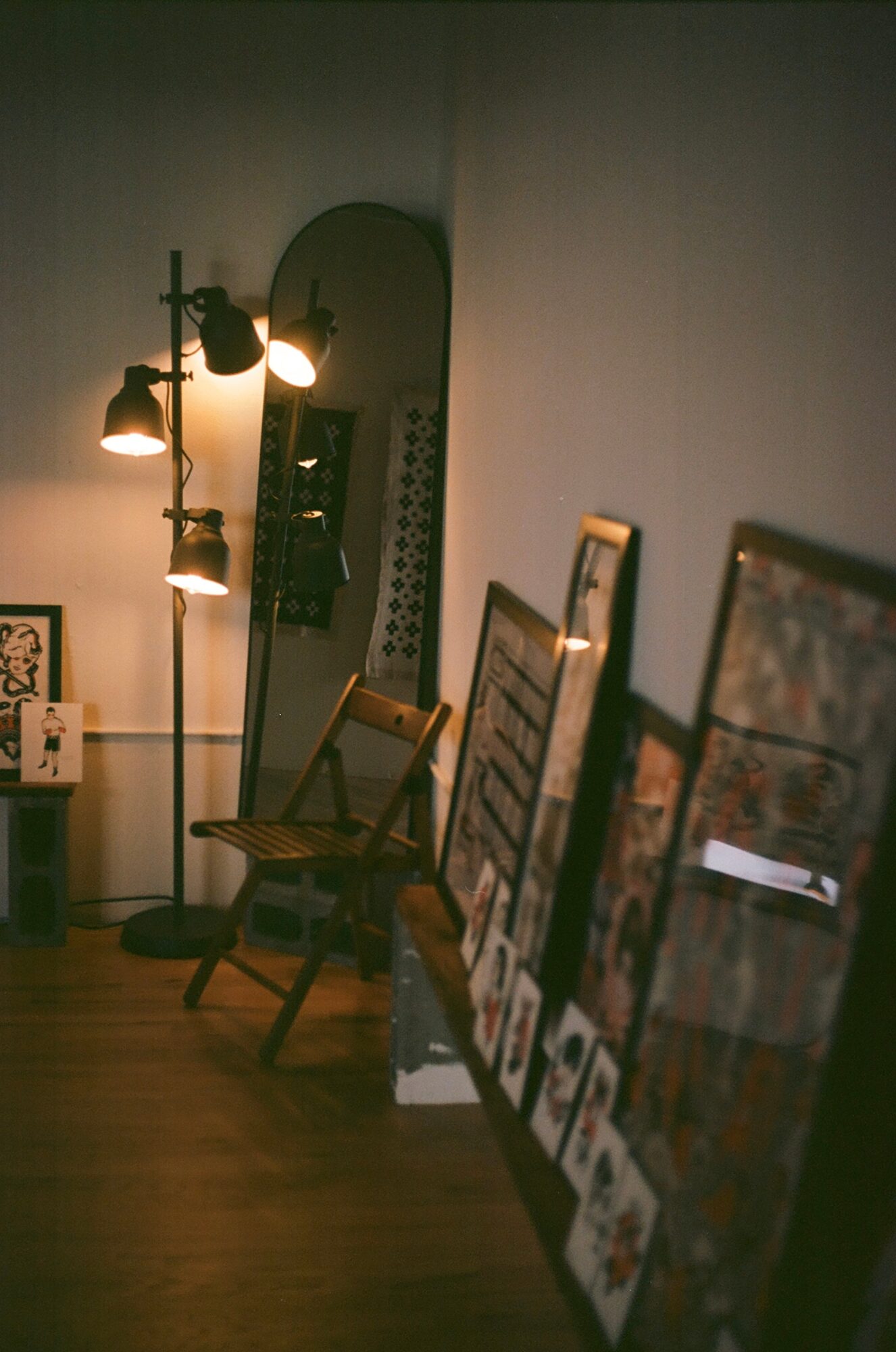 Room corner with framed artwork leaning against the wall, a mirror, a chair, and a floor lamp with multiple bulbs.