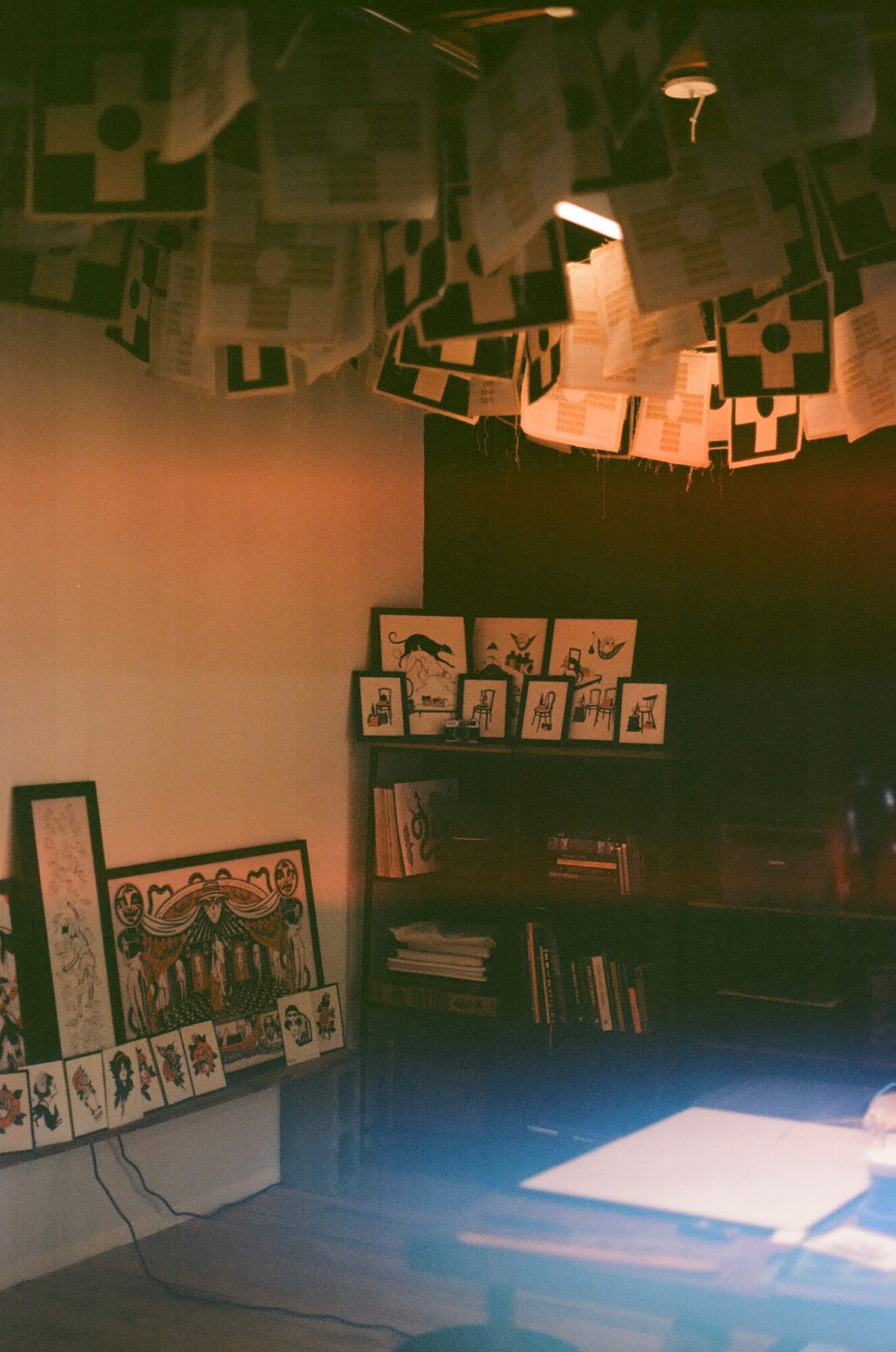 Room with hanging paper decorations, bookshelf with books, and framed artwork on the wall, illuminated by warm lighting.