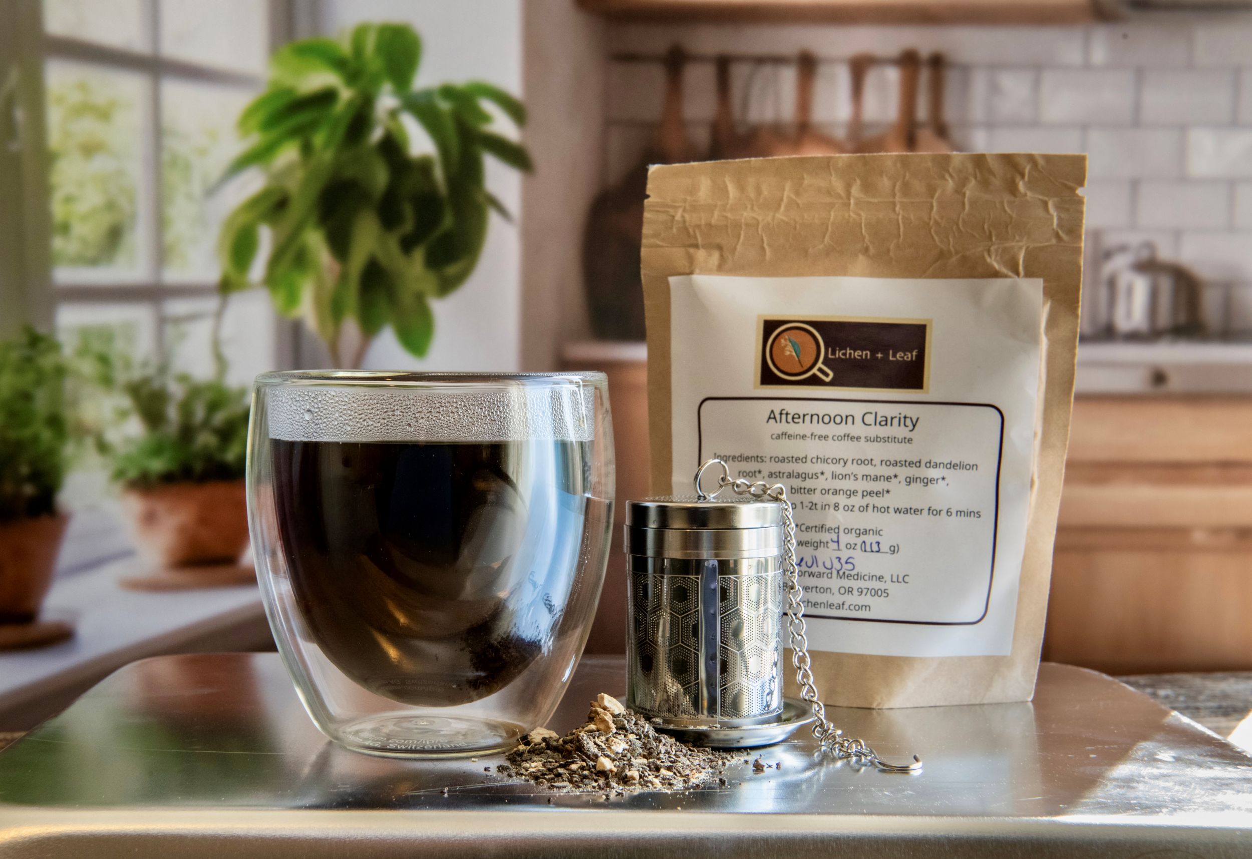 Glass cup filled with dark liquid, a metal scoop, and a paper bag labeled 'Afternoon Clarity' on a kitchen counter.