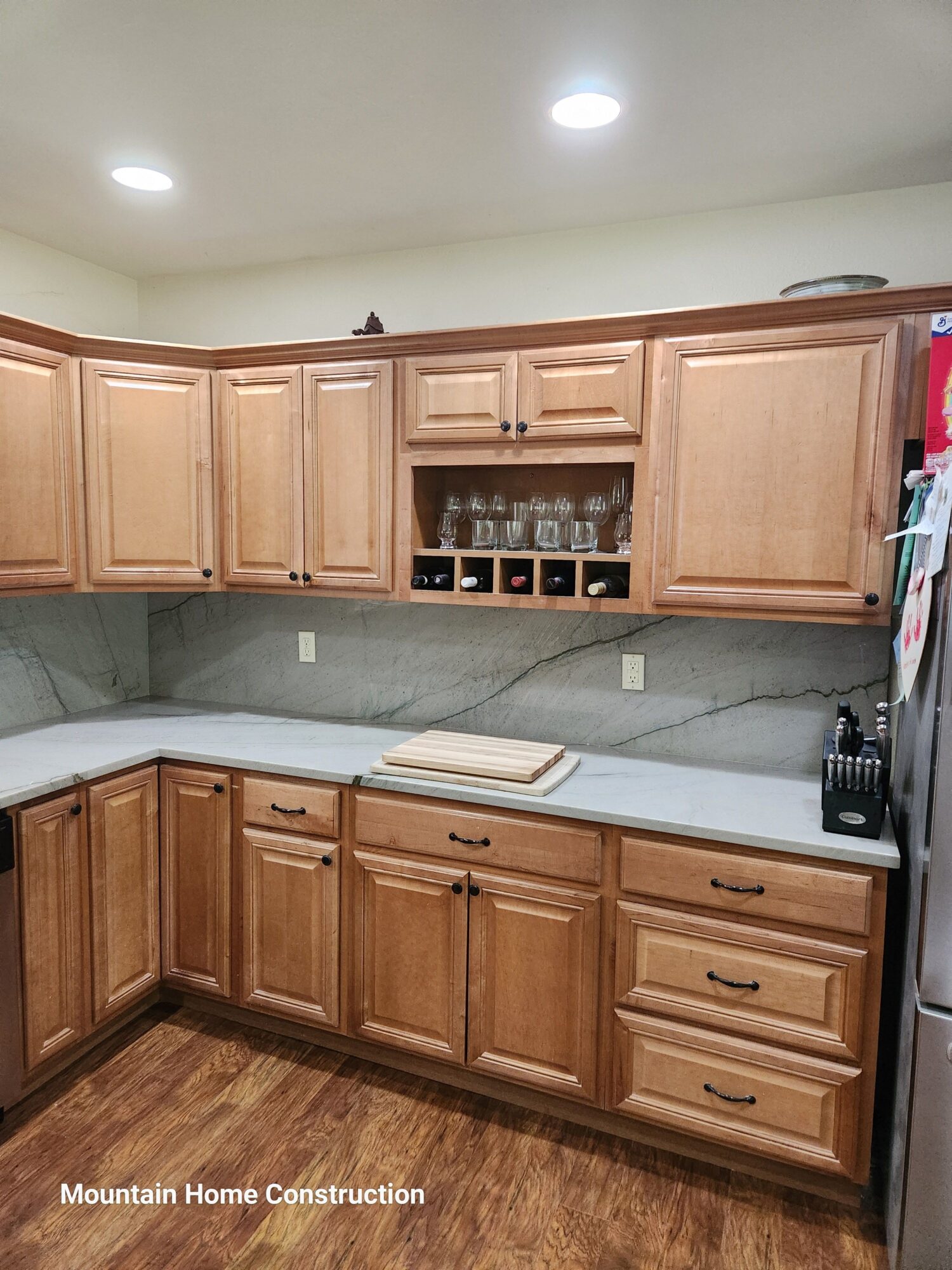 Wooden kitchen cabinets with wine rack, countertop, and drawers, with a wooden floor and gray wall in the background.