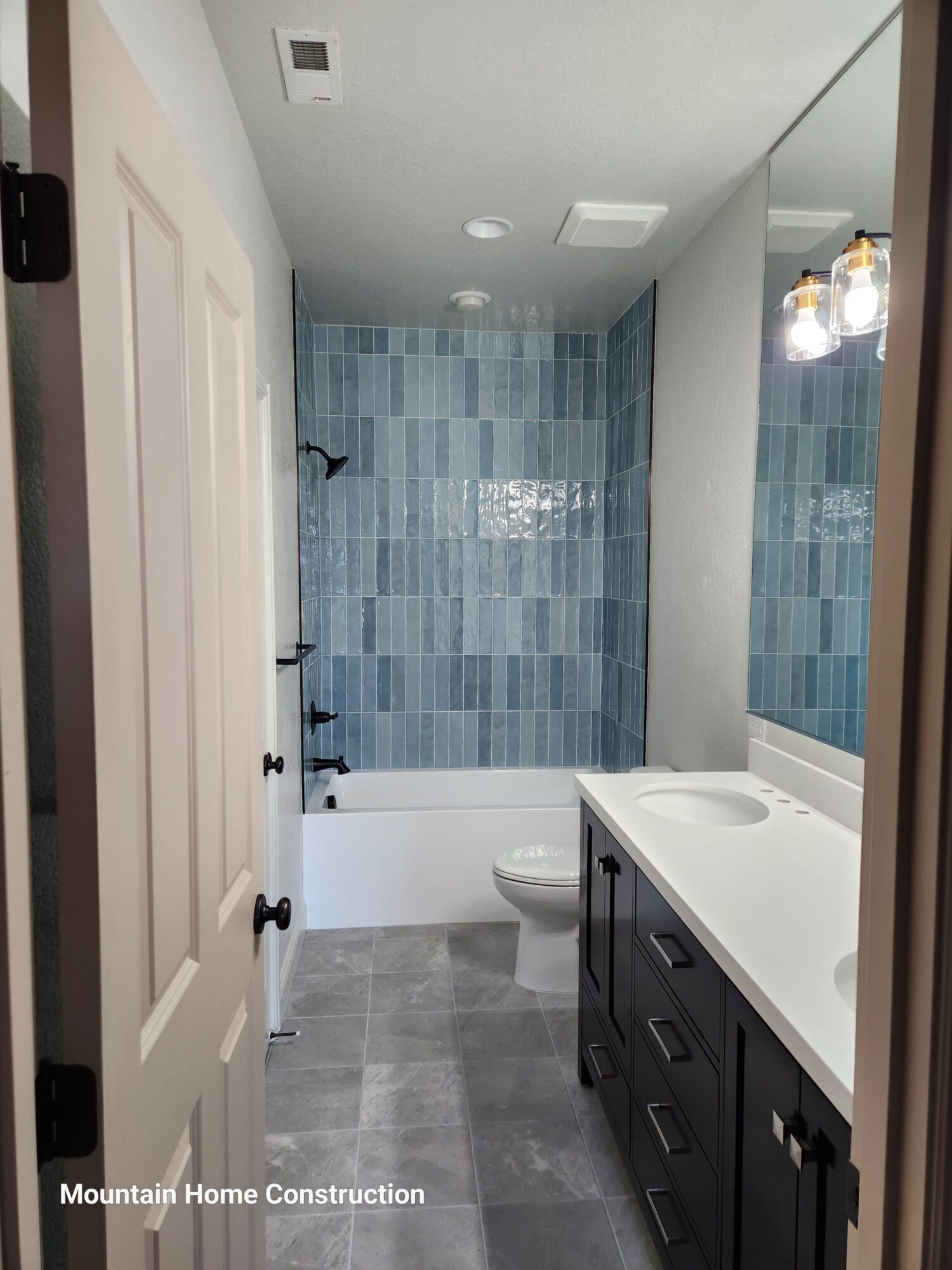 Bathroom with blue tiled wall, white vanity, and gray floor tiles, viewed from doorway.