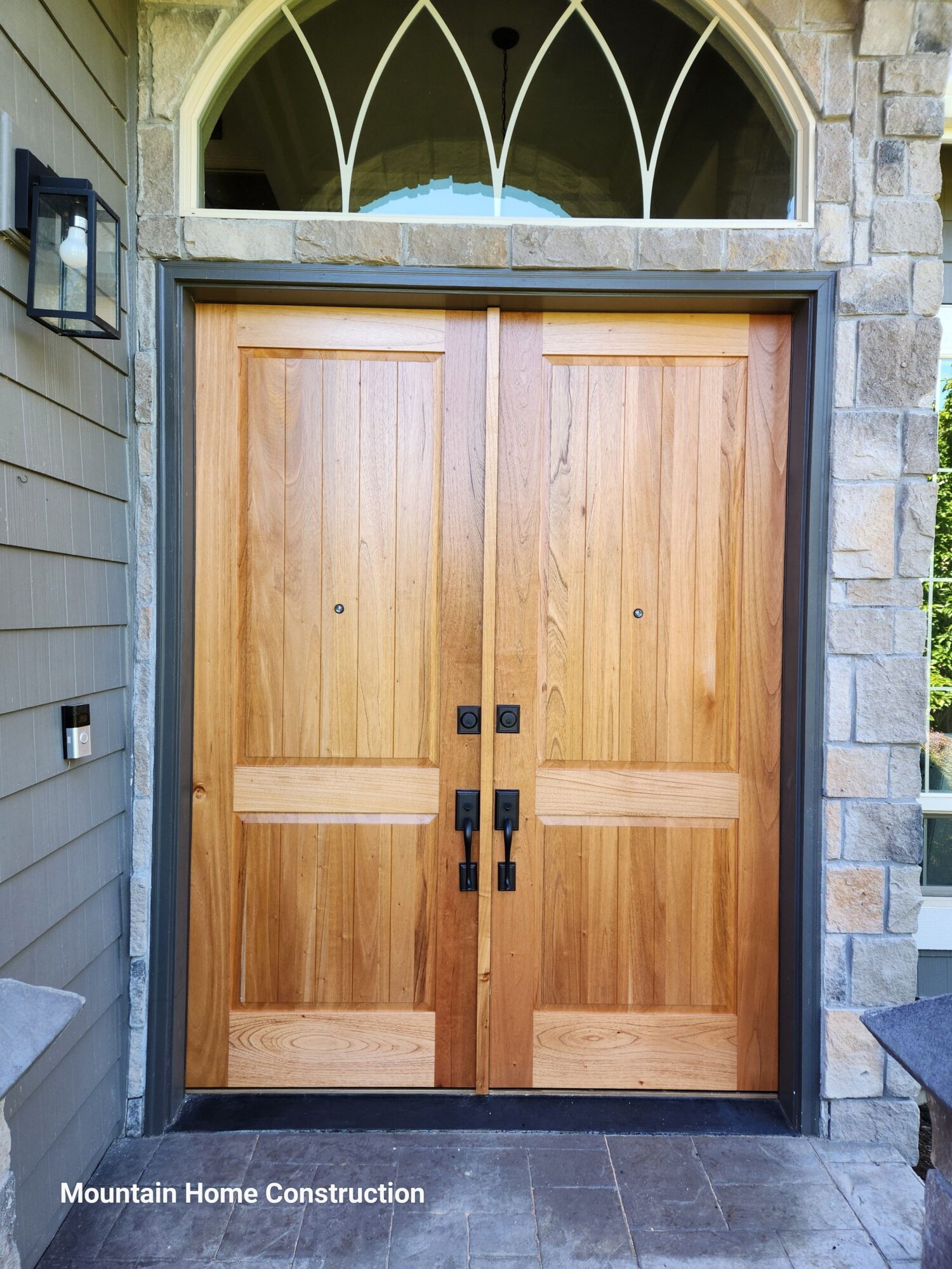 Wooden garage door with black handles, framed by stone and siding, viewed from below.