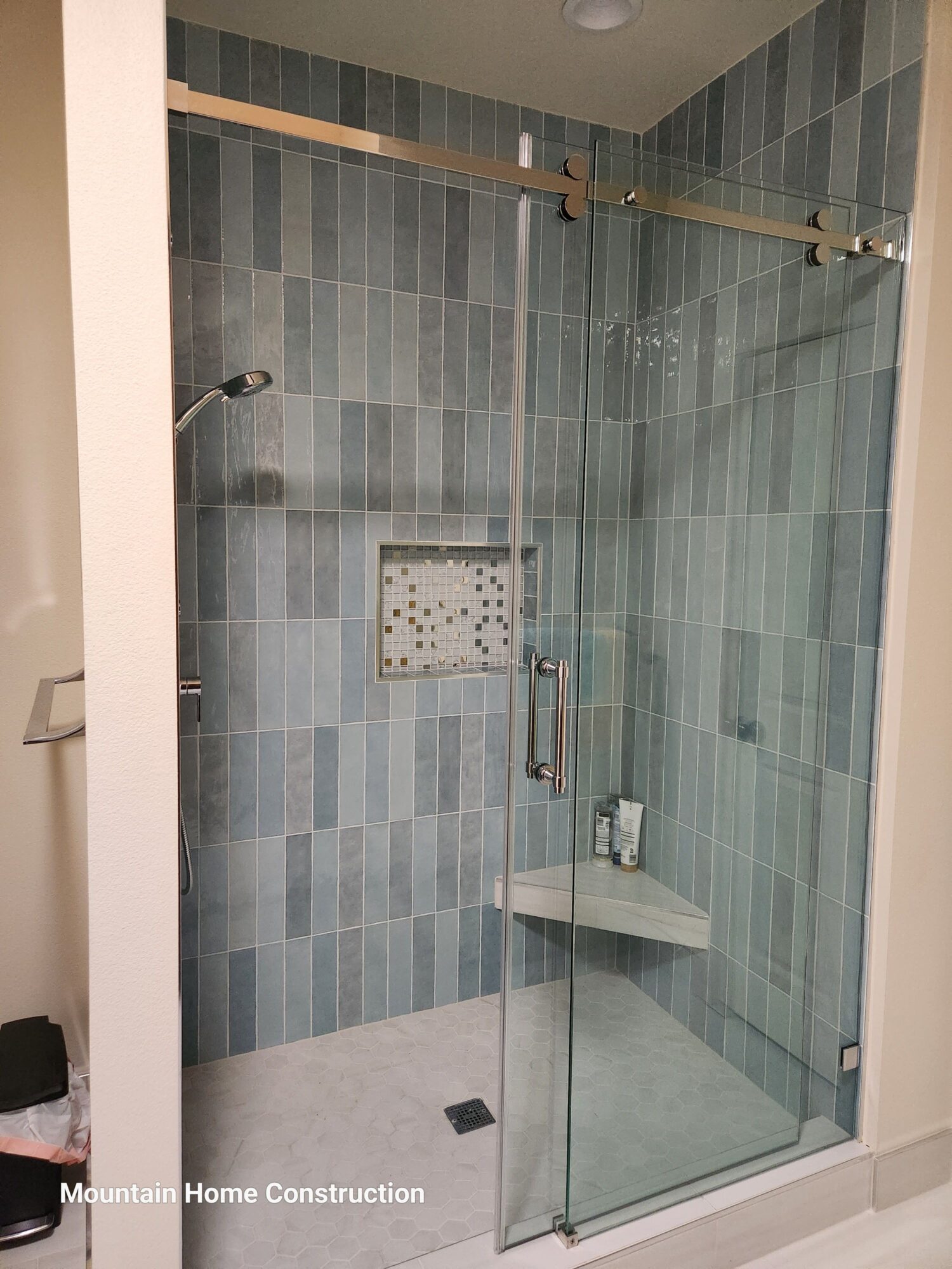 Shower area with glass door, tiled walls, and a drain on the floor.