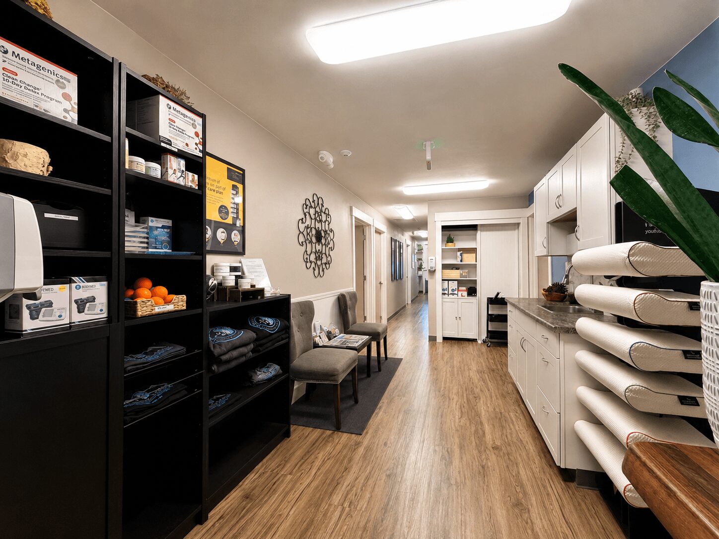 Long room with black shelves on the left, white cabinets on the right, wooden floor, and chairs at the end.