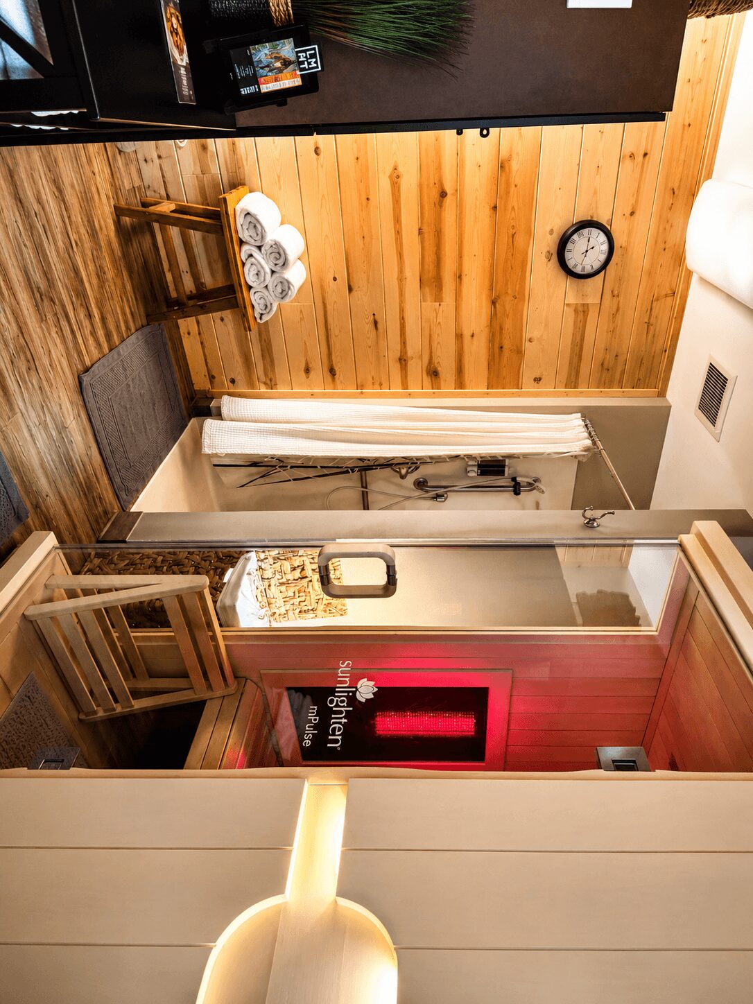 Interior of a room with wooden wall, clock, bench with towels, and a shower area with curtain.