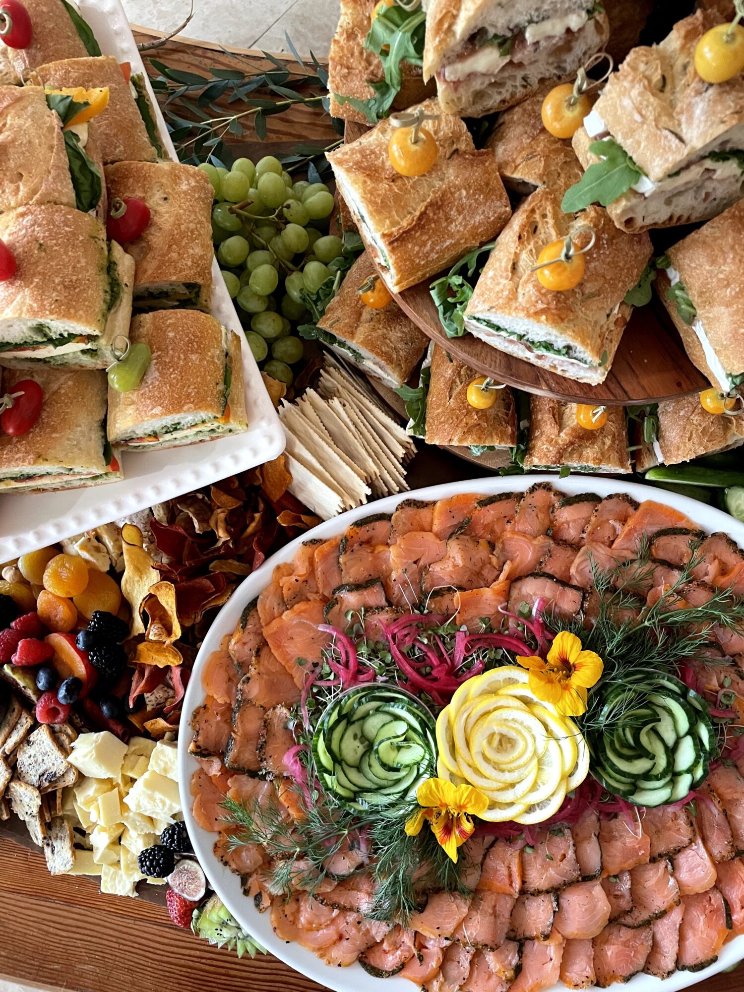 Assorted sandwiches, a platter of sliced meat with garnishes, and a cluster of green grapes on a table.
