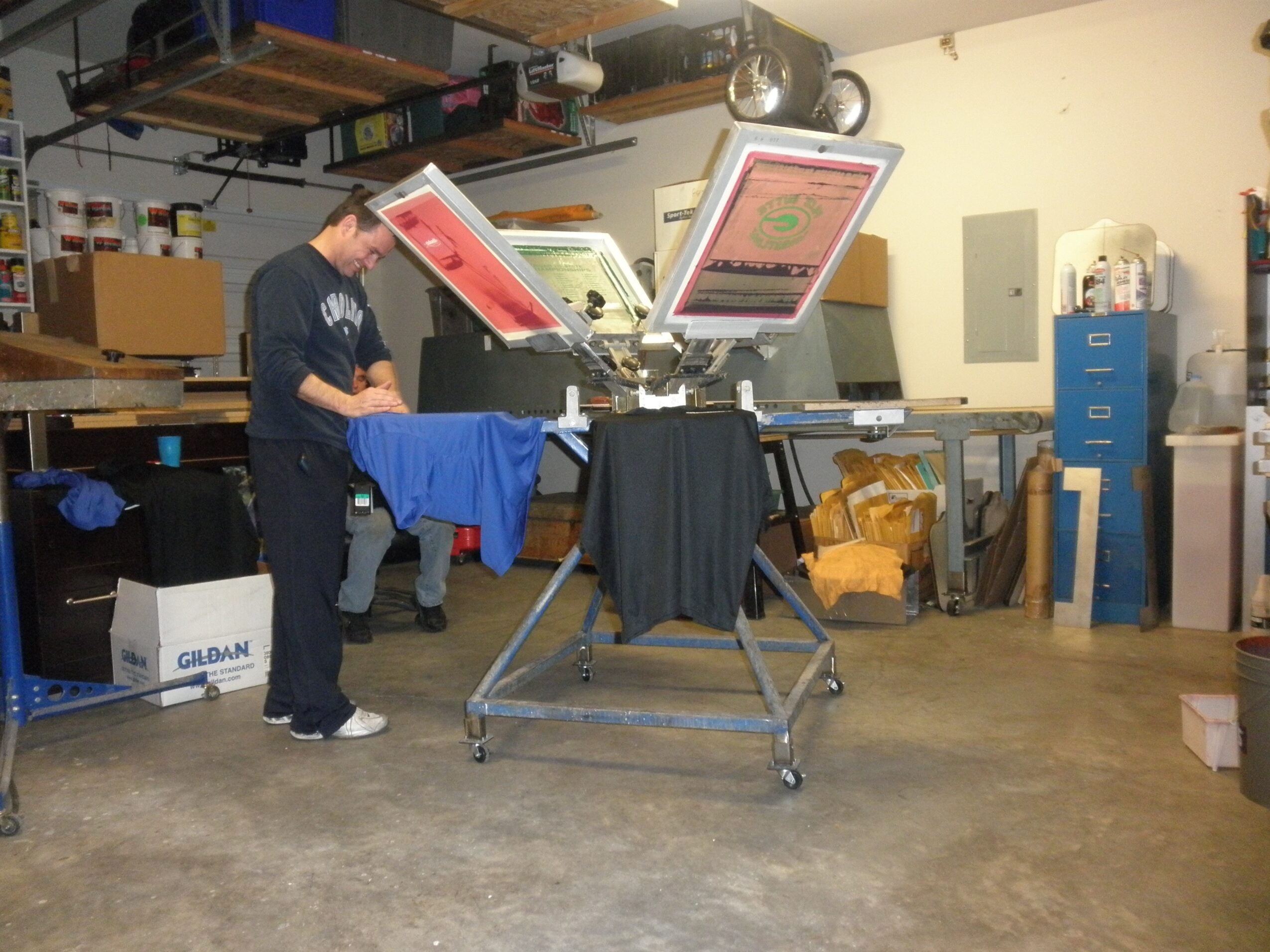 Person operating a large printing machine in a workshop with shelves and boxes around.