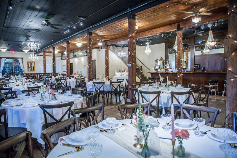 Elegant restaurant interior with tables set for dining, white tablecloths, floral centerpieces, and warm lighting, wooden beams, and decor.