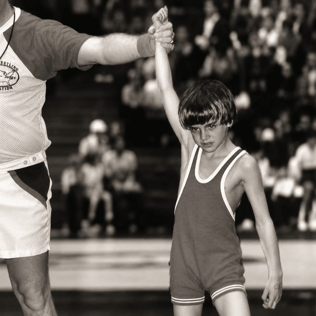 Young boy in a sports uniform being awarded a medal or trophy by an adult, with a crowd in the background.