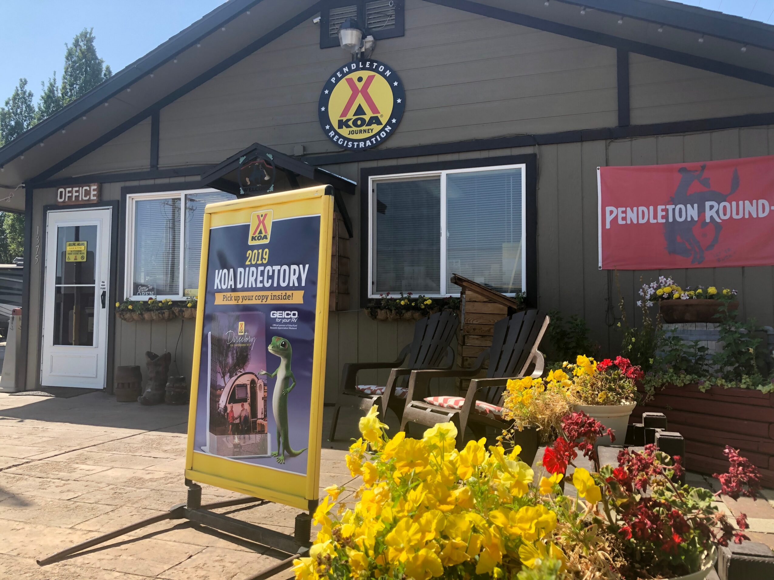 Building with a sign, window, flowers, and a yellow directory stand outside, under a clear sky.