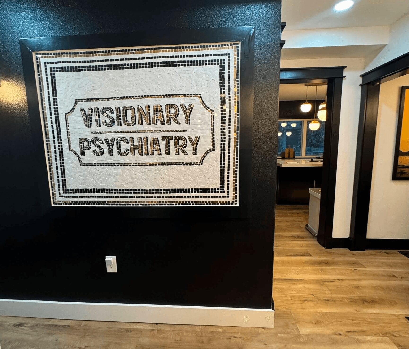 Mosaic sign reads 'Visionary Psychiatry' on a black wall, with a hallway and framed artwork visible in the background.