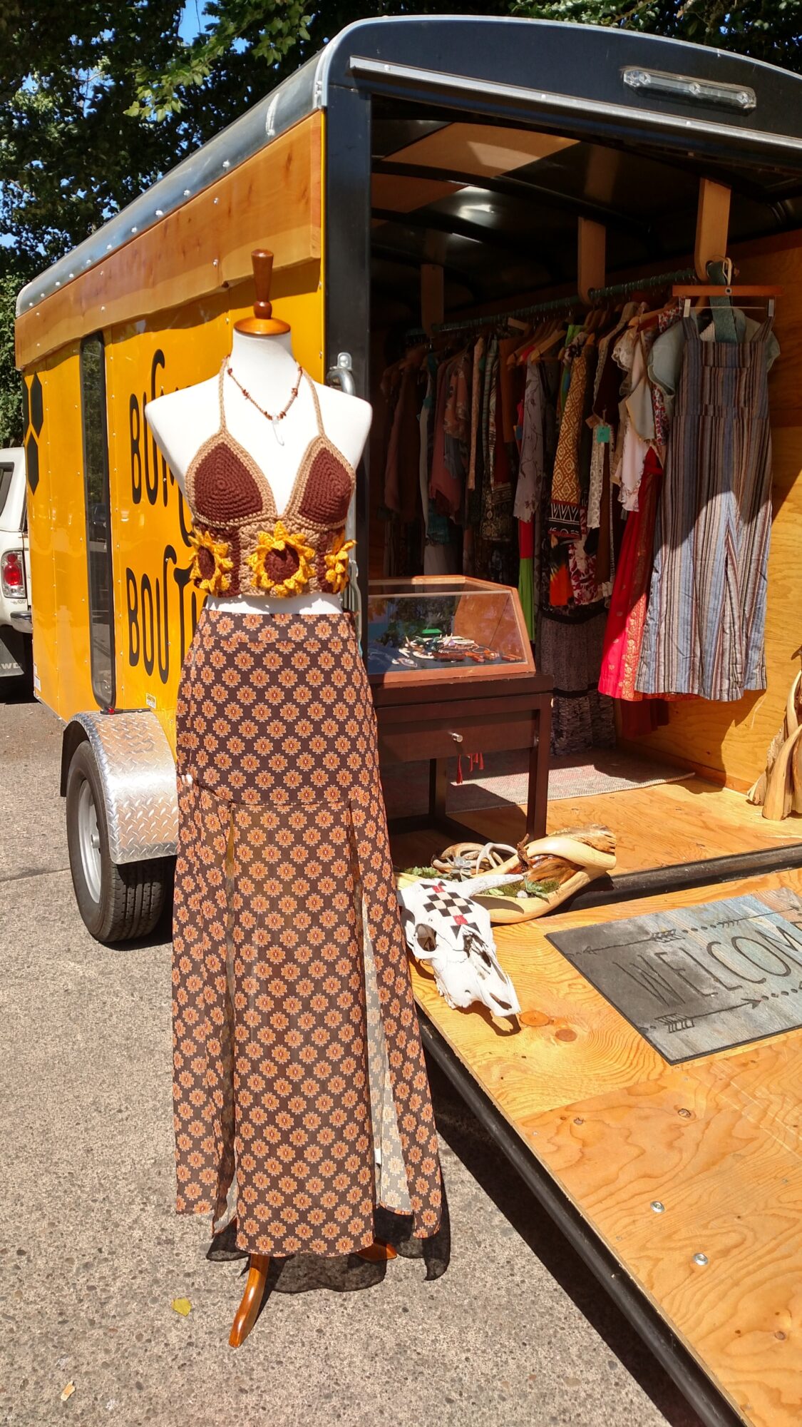 Mannequin wearing a long patterned dress with a belt, displayed outside a vintage clothing truck.