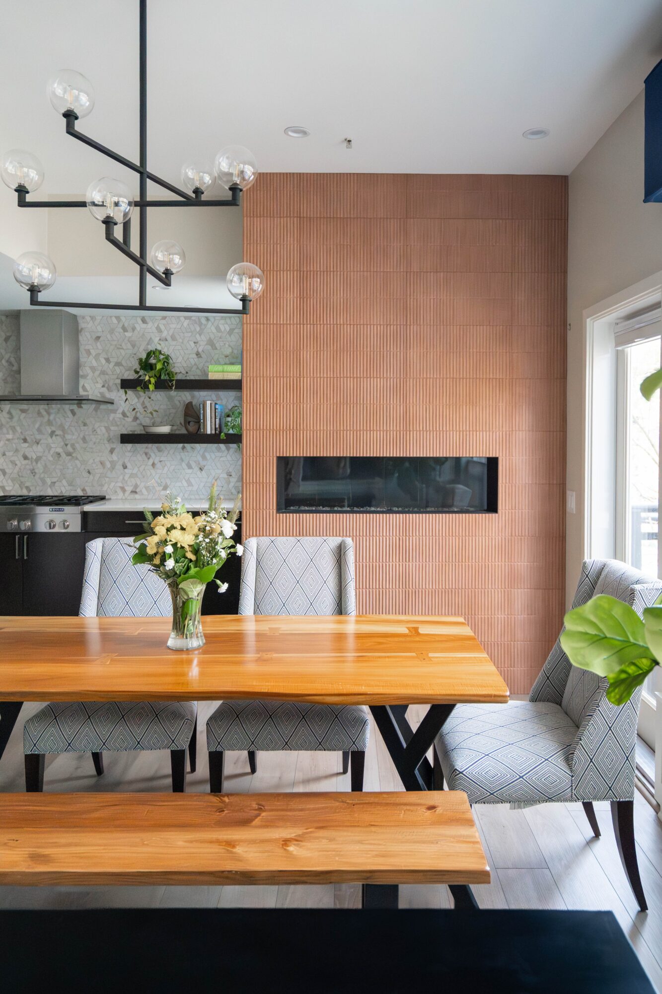 Dining area with wooden table, gray chairs, and a fireplace on a brick wall, with a window and modern decor.