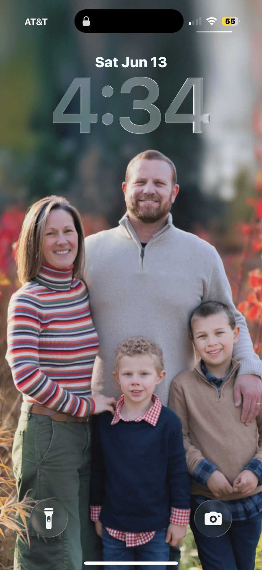 Family of five outdoors, smiling, with trees and sunlight in background.