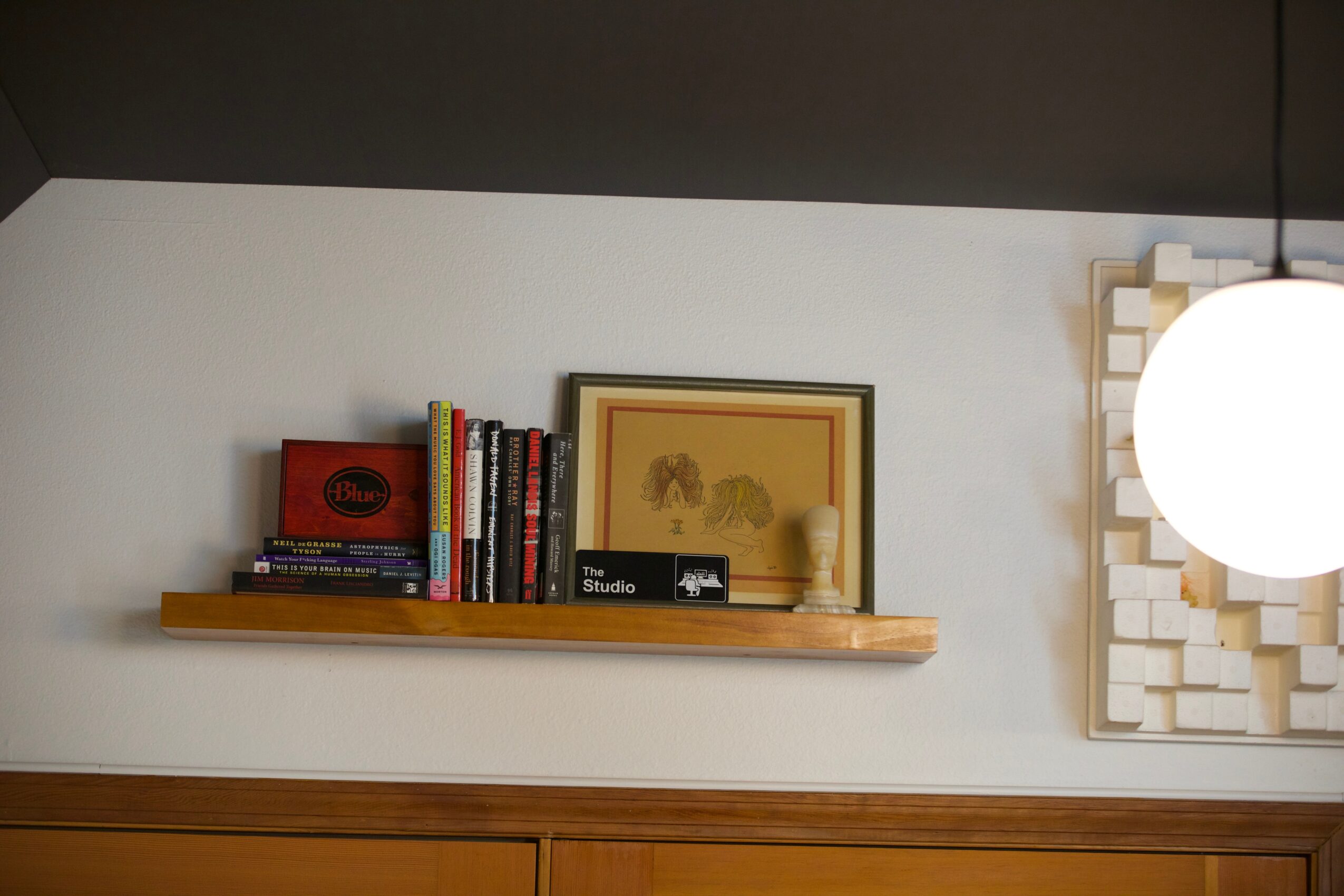 Bookshelf with books, framed picture, and decorative items on a wall-mounted shelf.