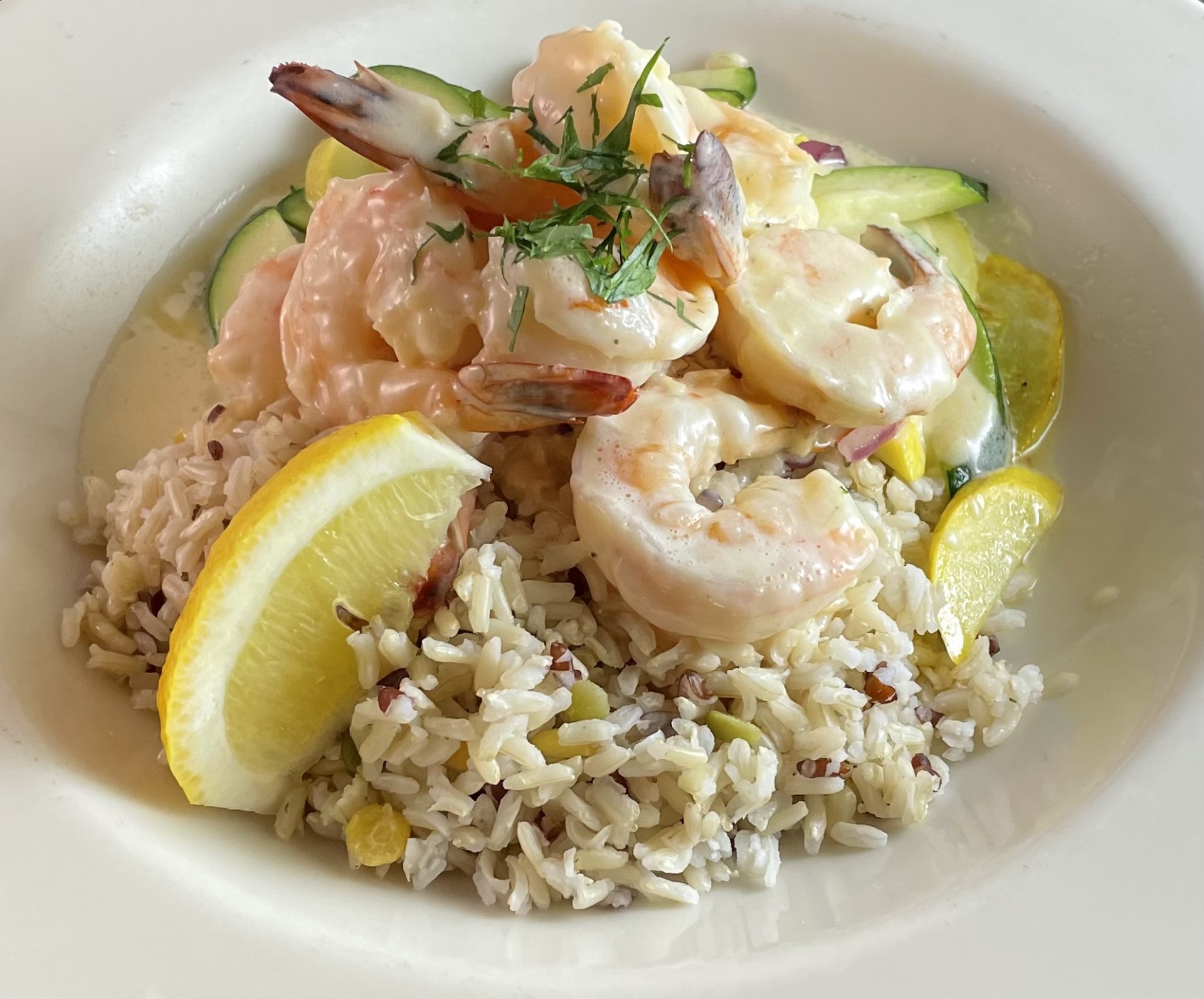 Shrimp and rice dish with lemon wedges, cucumber slices, and herbs in a white bowl.