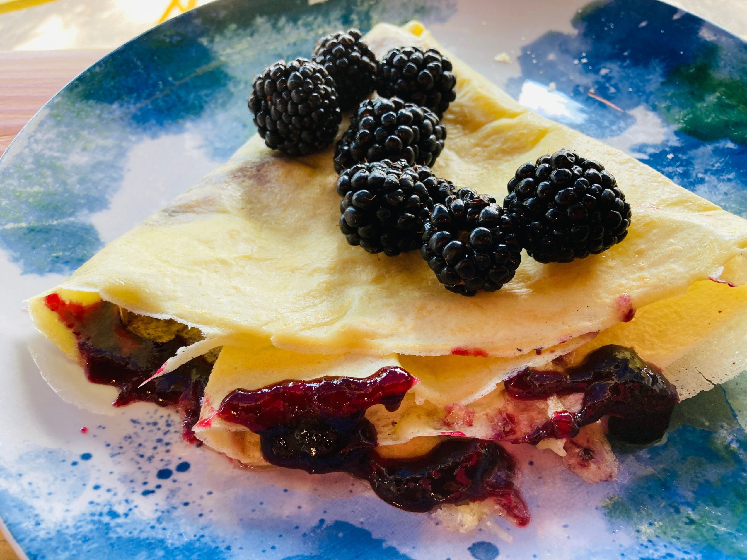 Slice of berry-filled dessert topped with blackberries on a colorful plate.