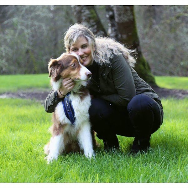 Woman crouching on grass with a dog outdoors, smiling, trees in background