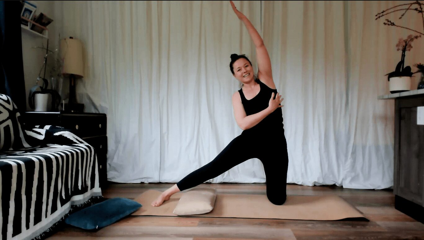Person practicing ballet or dance pose on a mat in a room with curtains, a couch, and a side table.
