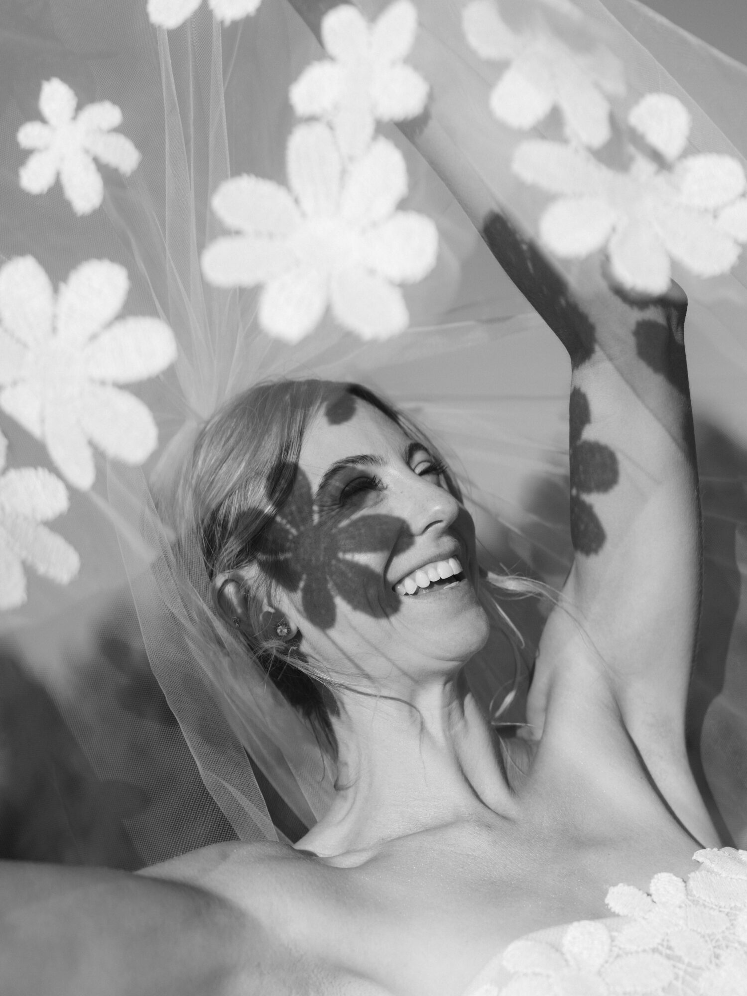 Smiling woman with short hair, surrounded by flower-shaped shadows, holding an umbrella, in black and white.