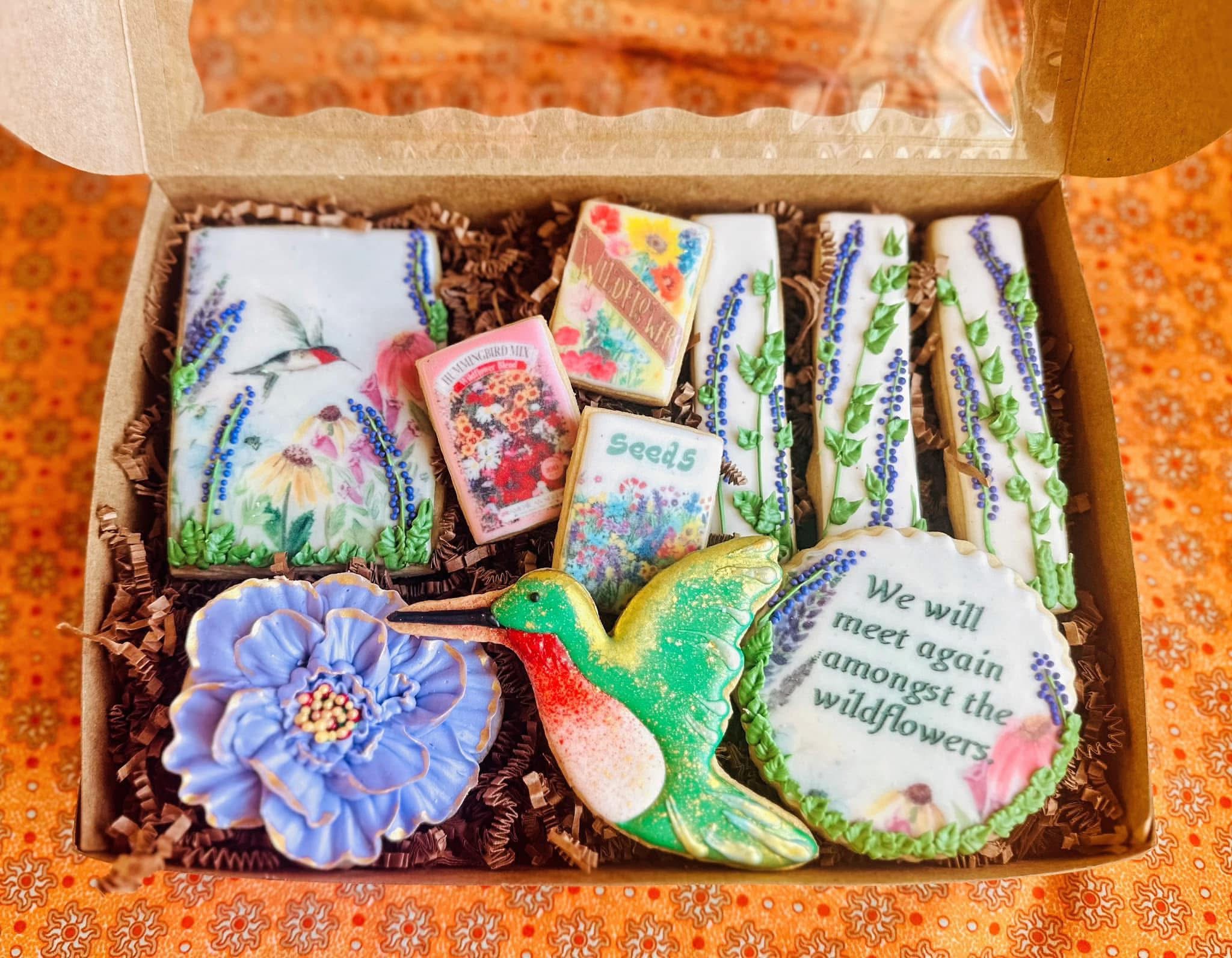 Open box with decorated cookies, a small box, and a colorful bird-shaped cookie, on an orange patterned surface.