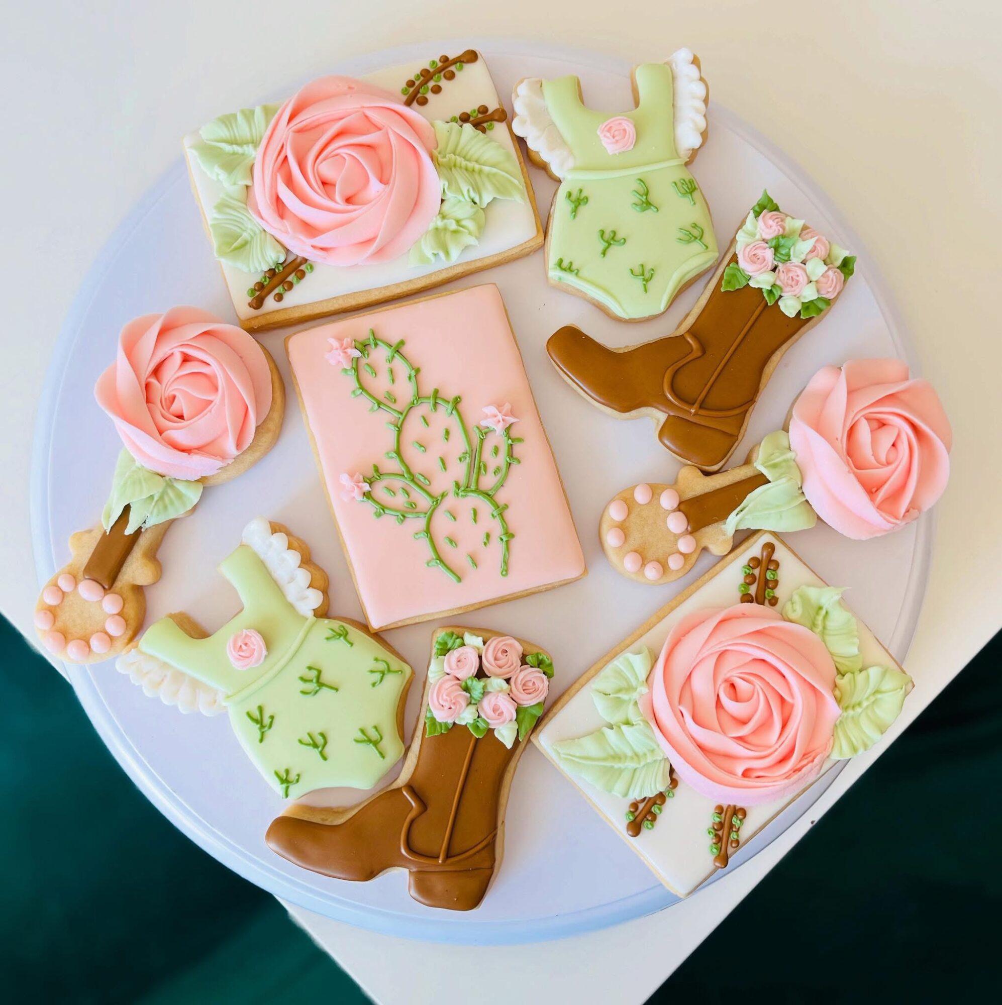 Decorative cookies with roses, cactus, and boots on a white plate, featuring pastel colors and floral details.