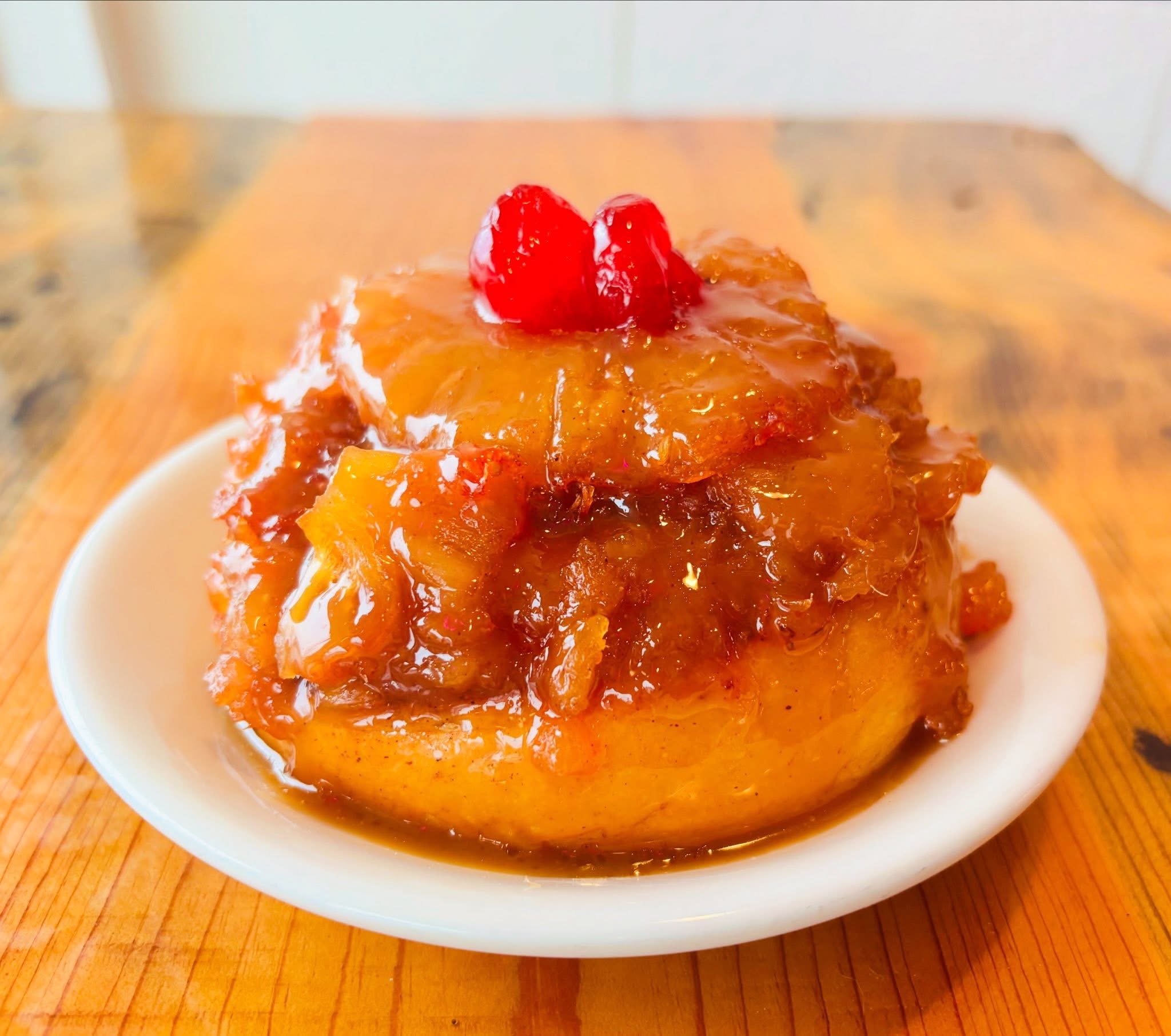 A dessert topped with red berries and caramelized fruit on a small white plate, placed on a wooden surface.
