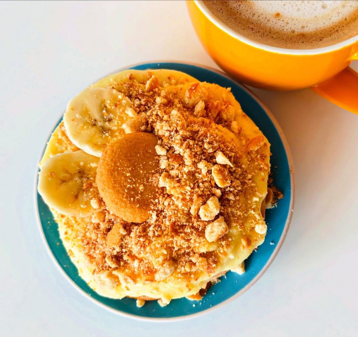 Banana slices and a cookie on a plate with a cup of coffee nearby, viewed from above.