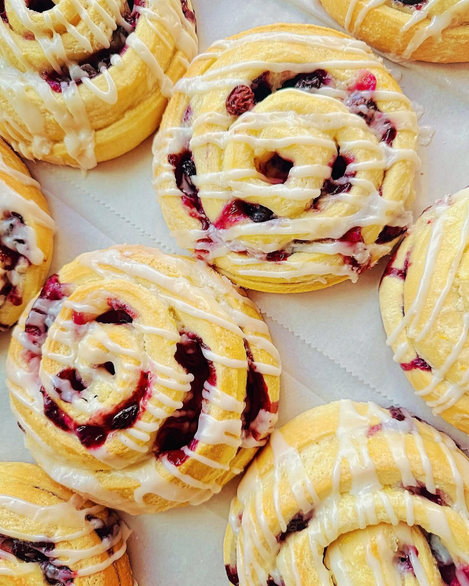Close-up of berry-filled pastries with yellow icing and drizzle, arranged on a white surface.
