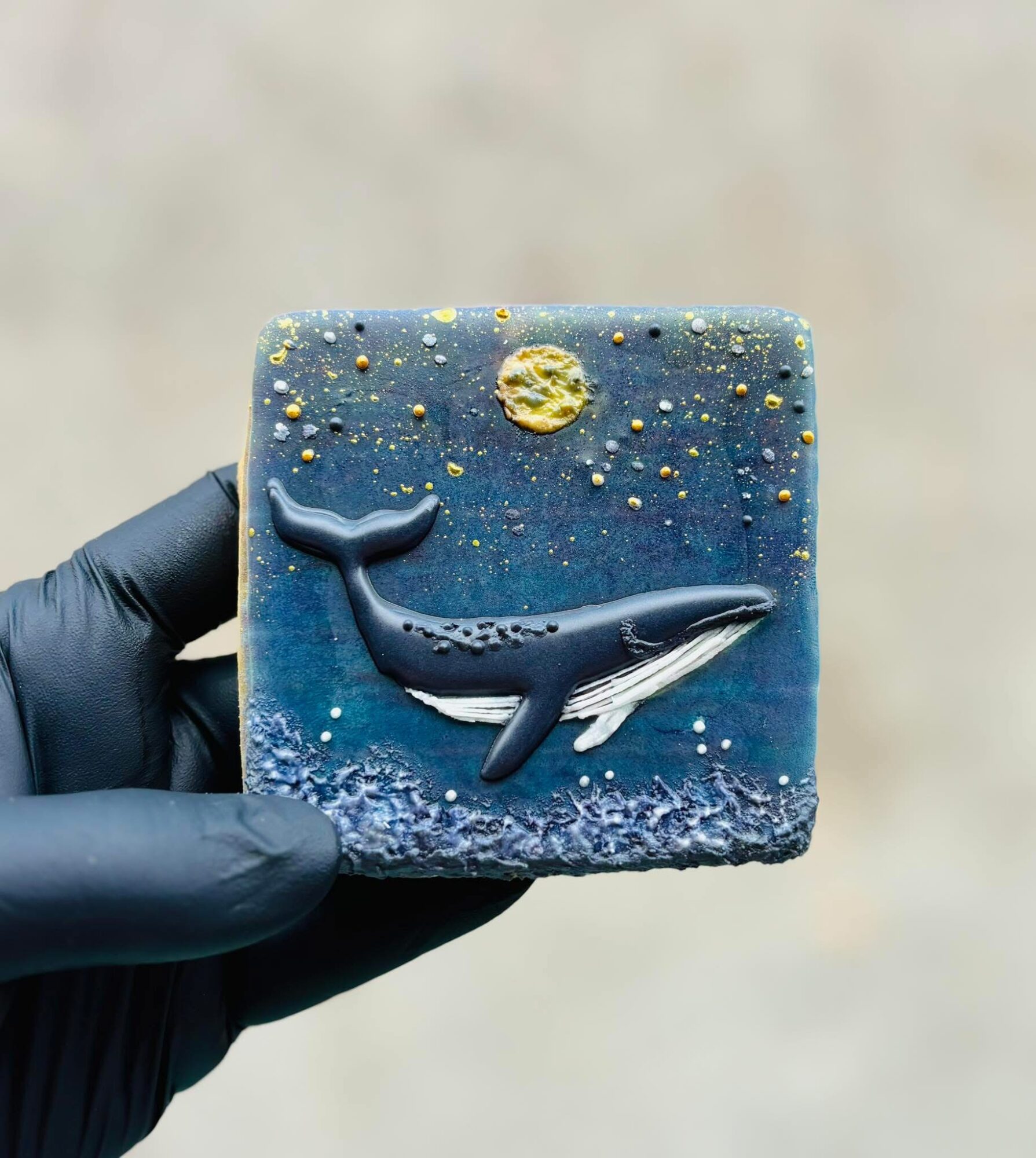 Square soap with whale and night sky design, including moon and stars, held by a gloved hand.