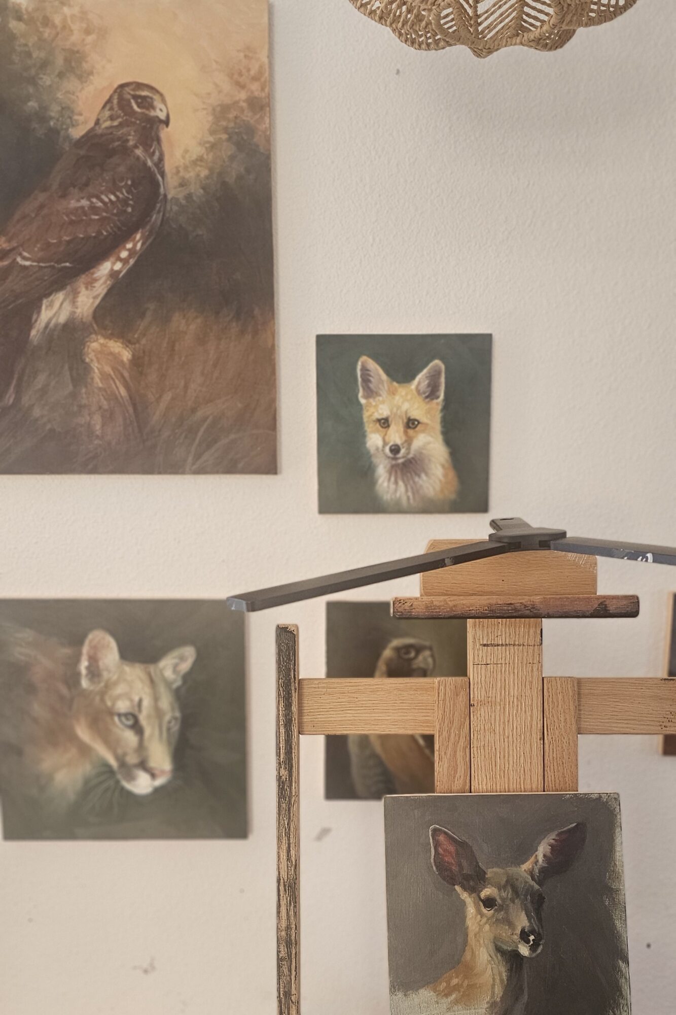 Four animal paintings on a wall, including a fox, a wolf, a bird, and a deer, with a wooden structure in front.