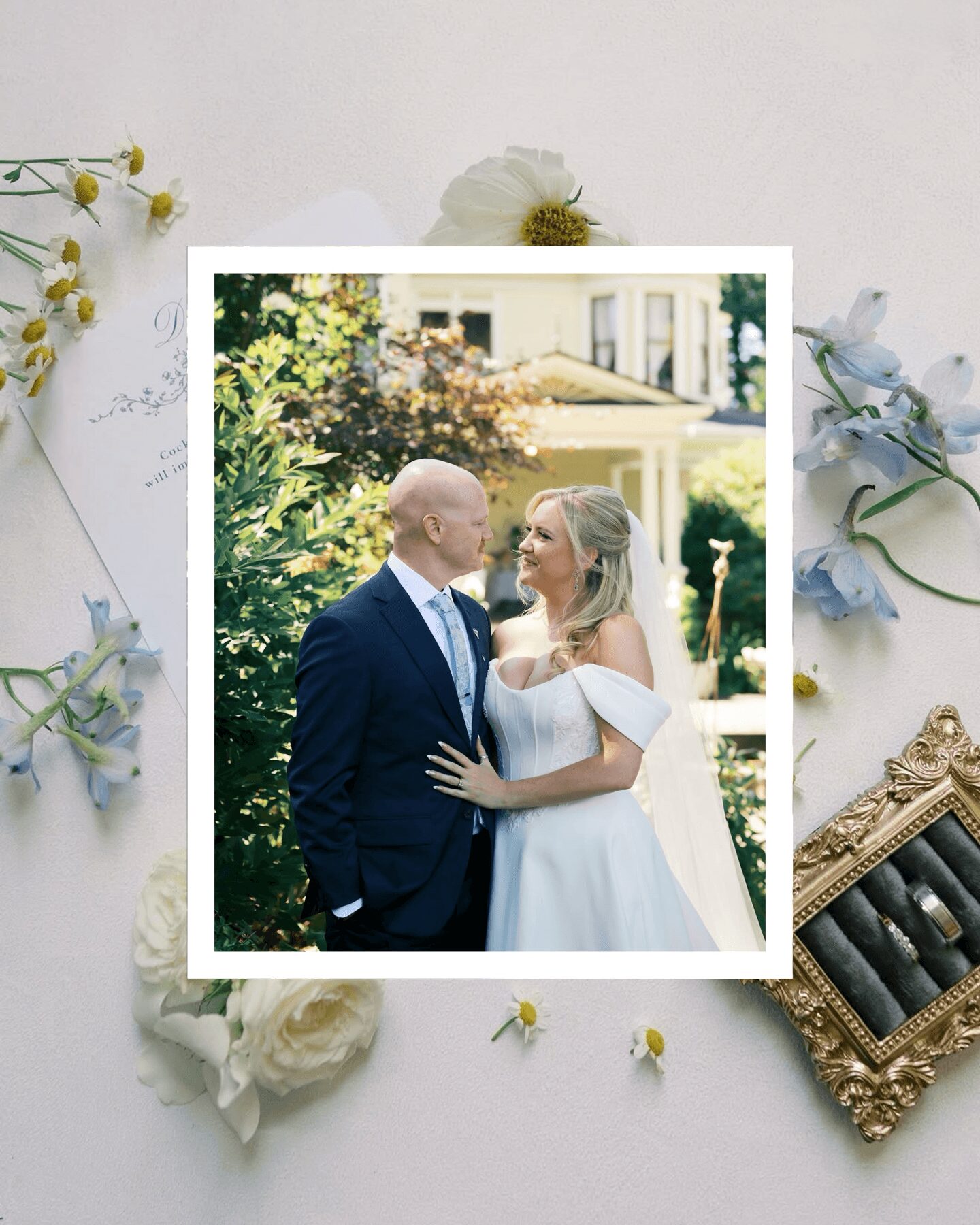 A couple in wedding attire standing outdoors, gazing at each other, surrounded by greenery and a building in the background.
