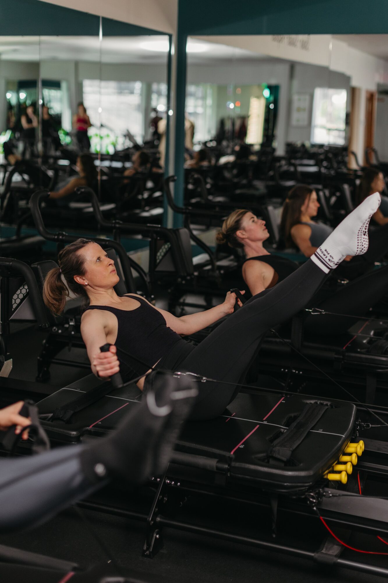 Group of women exercising on reformer machines in a fitness studio with mirrors and large windows