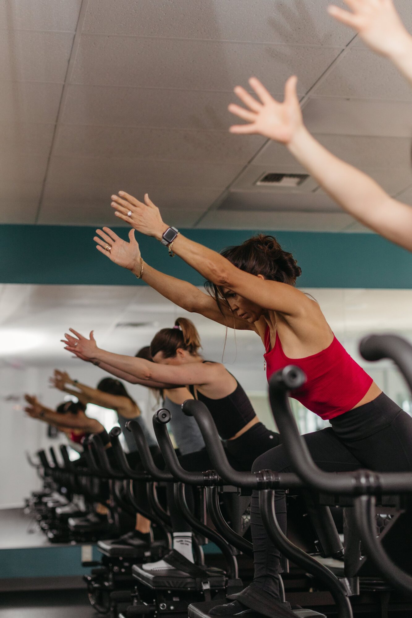 People exercising on treadmills with arms raised, in a gym setting, ceiling visible, some faces visible, group workout.