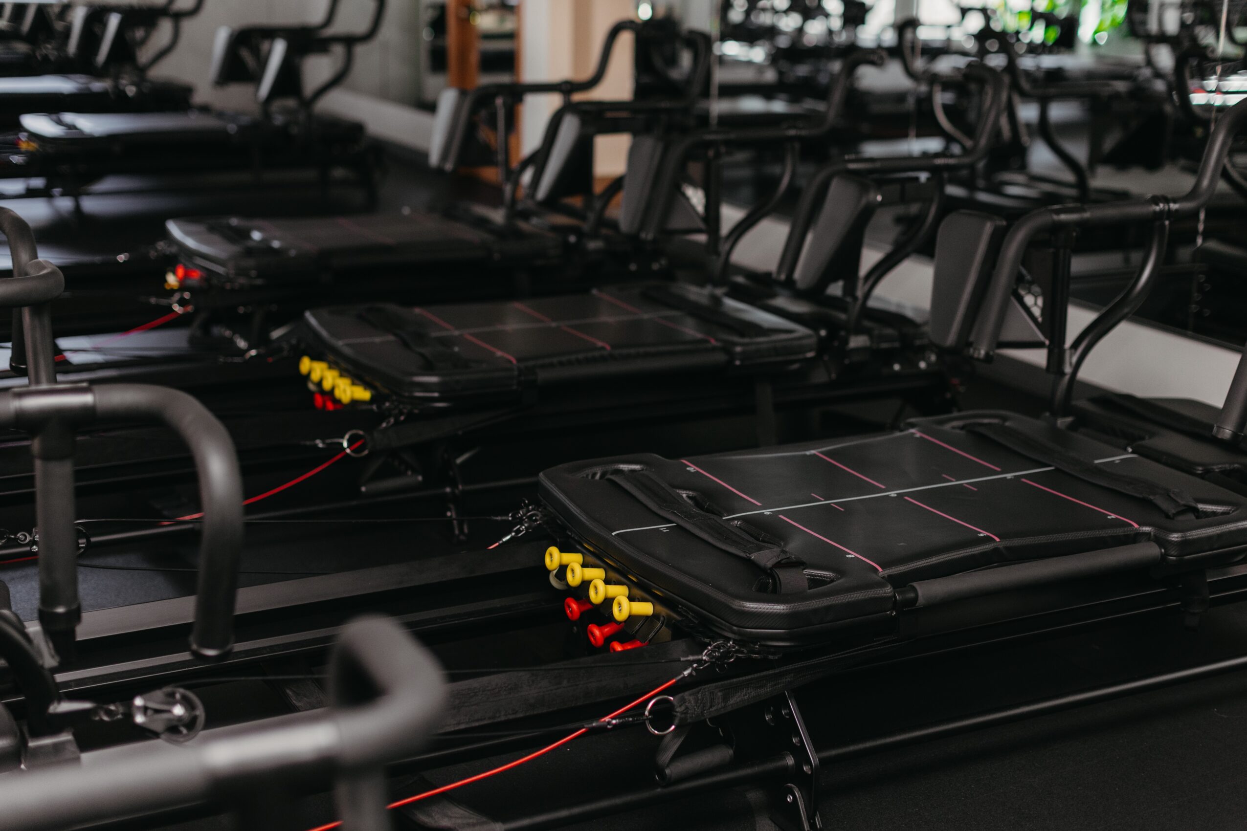 Multiple black exercise machines in a gym, with some yellow and red safety features visible, arranged in rows.